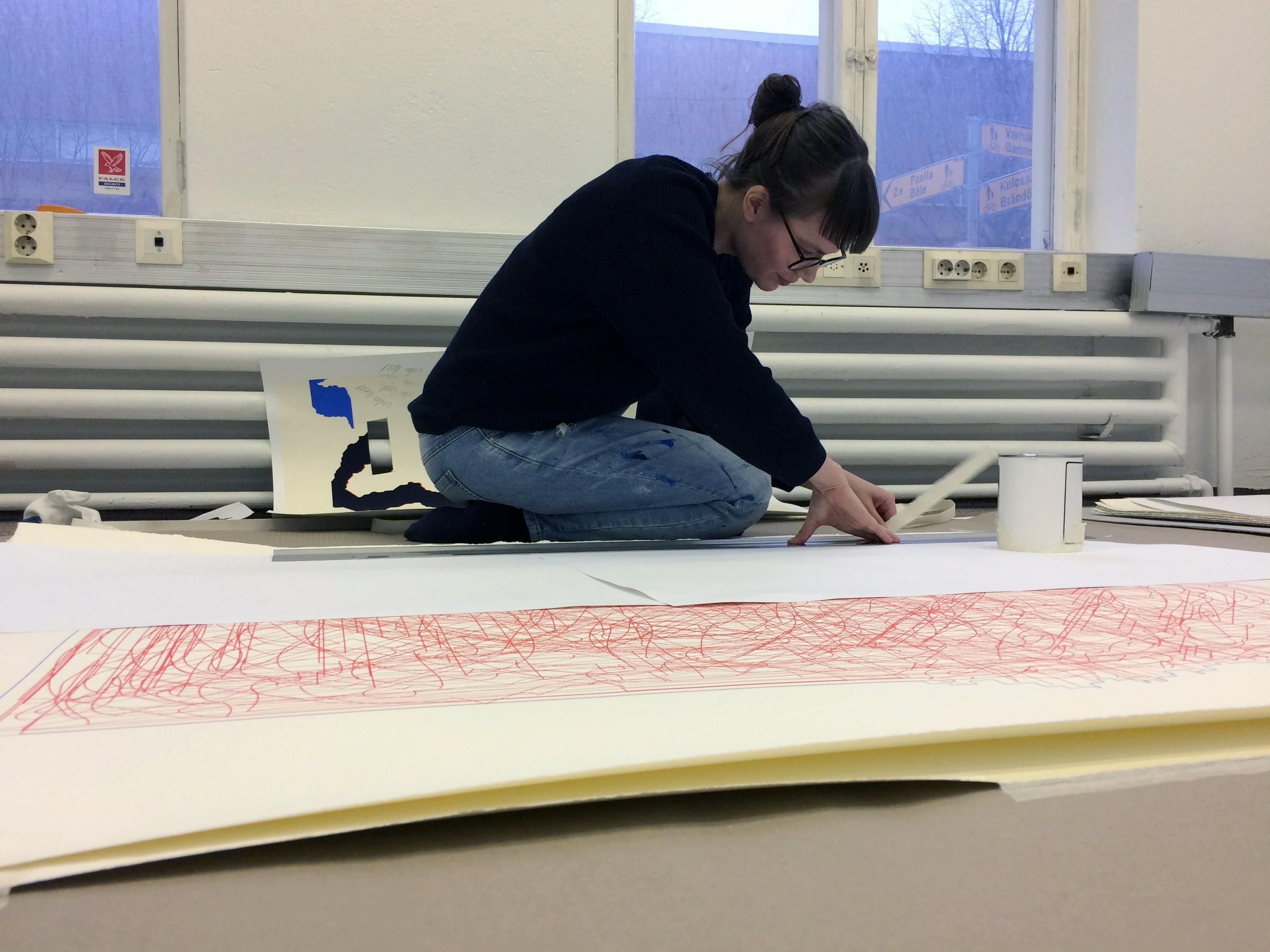 Artist Inka Bell crouching on the floor and working on a large print in her Helsinki studio.