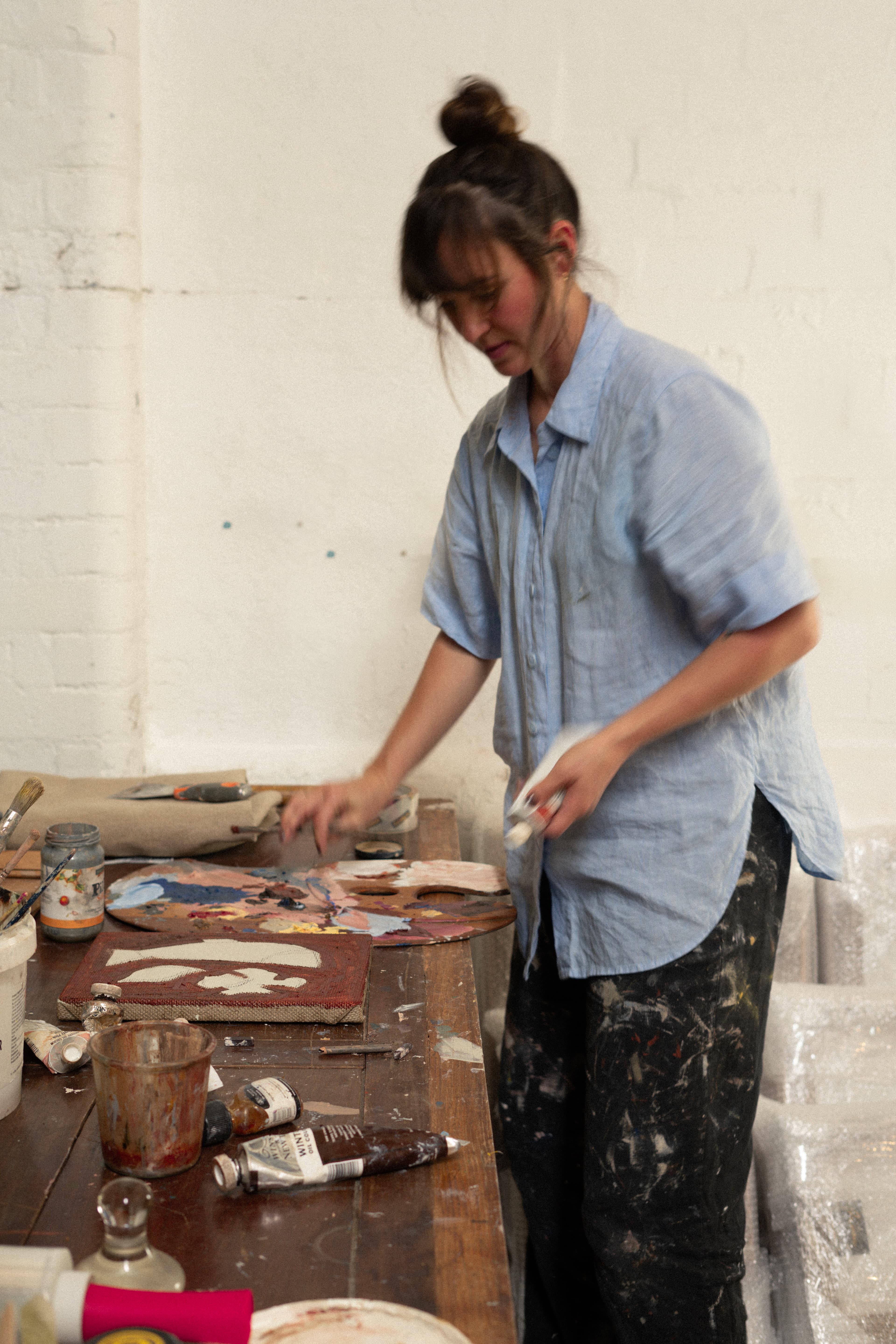 Artist Brittany Ferns painting a small, brown painting with a fish in her studio.