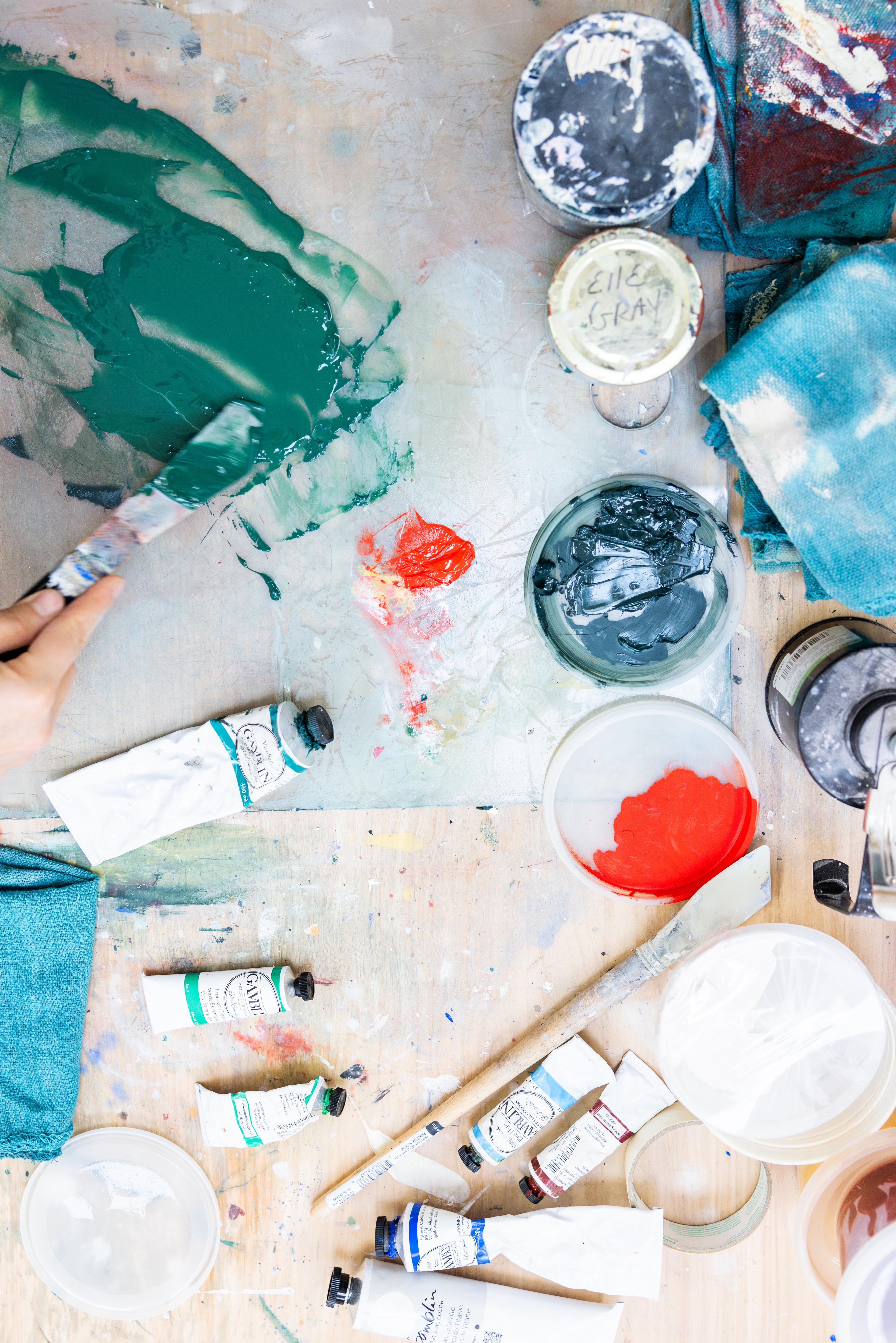 Paint tubes and various tools laid out on a surface in artist Arielle Zamora's studio.