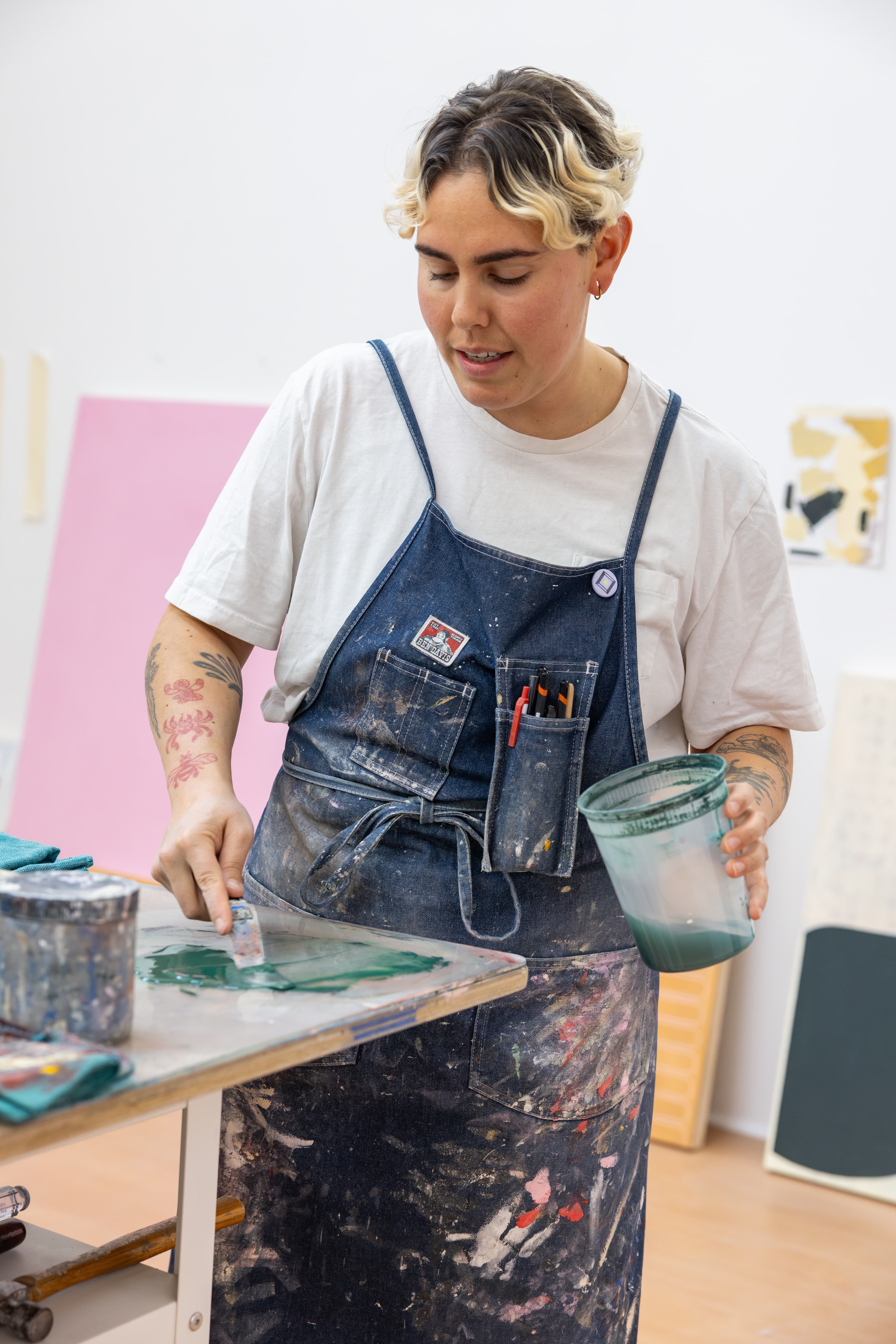 Artist Arielle Zamora mixing green paint in their studio/