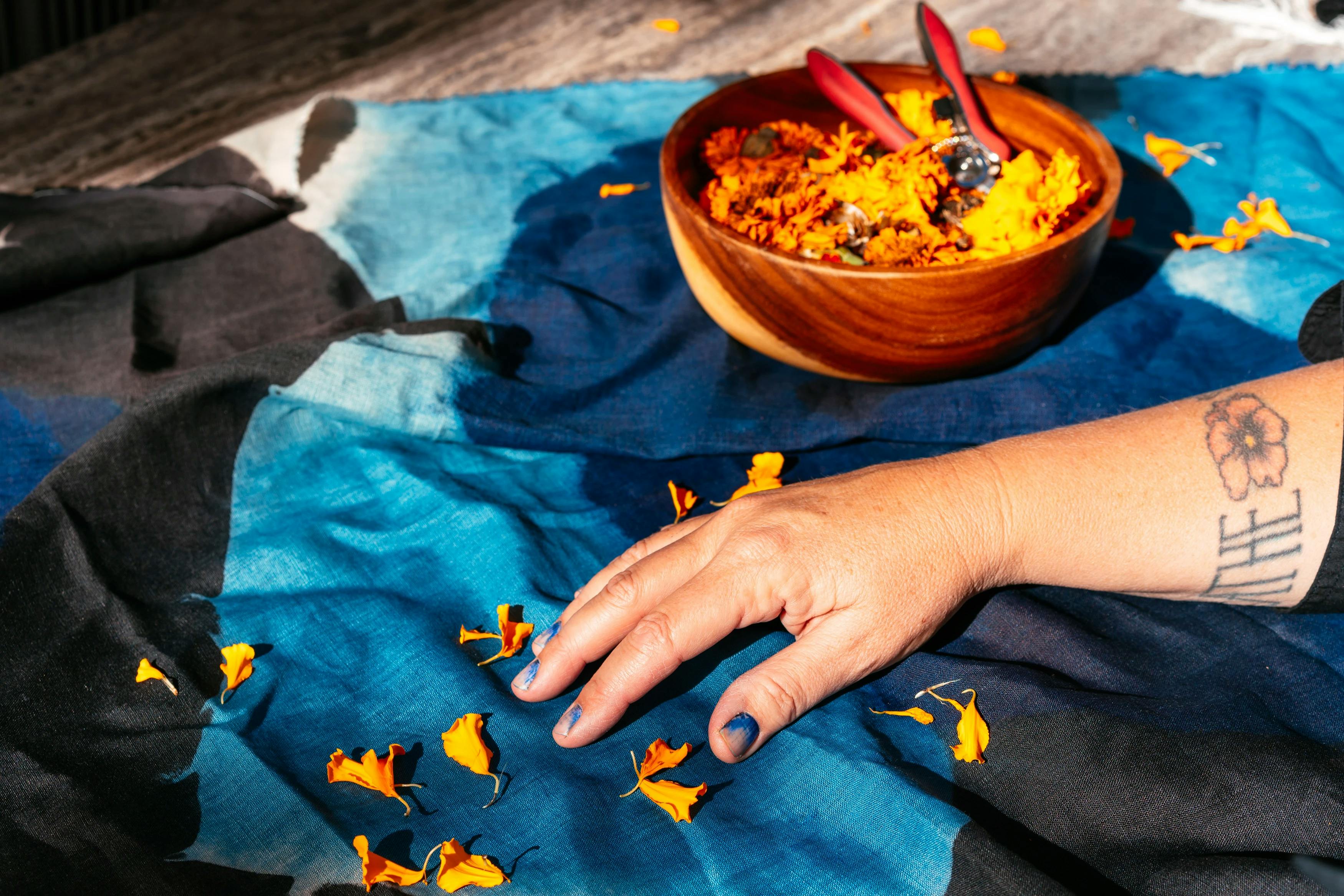 Artist Carrie Crawford's hands next to dyed fabric and a bowl of flowers. 