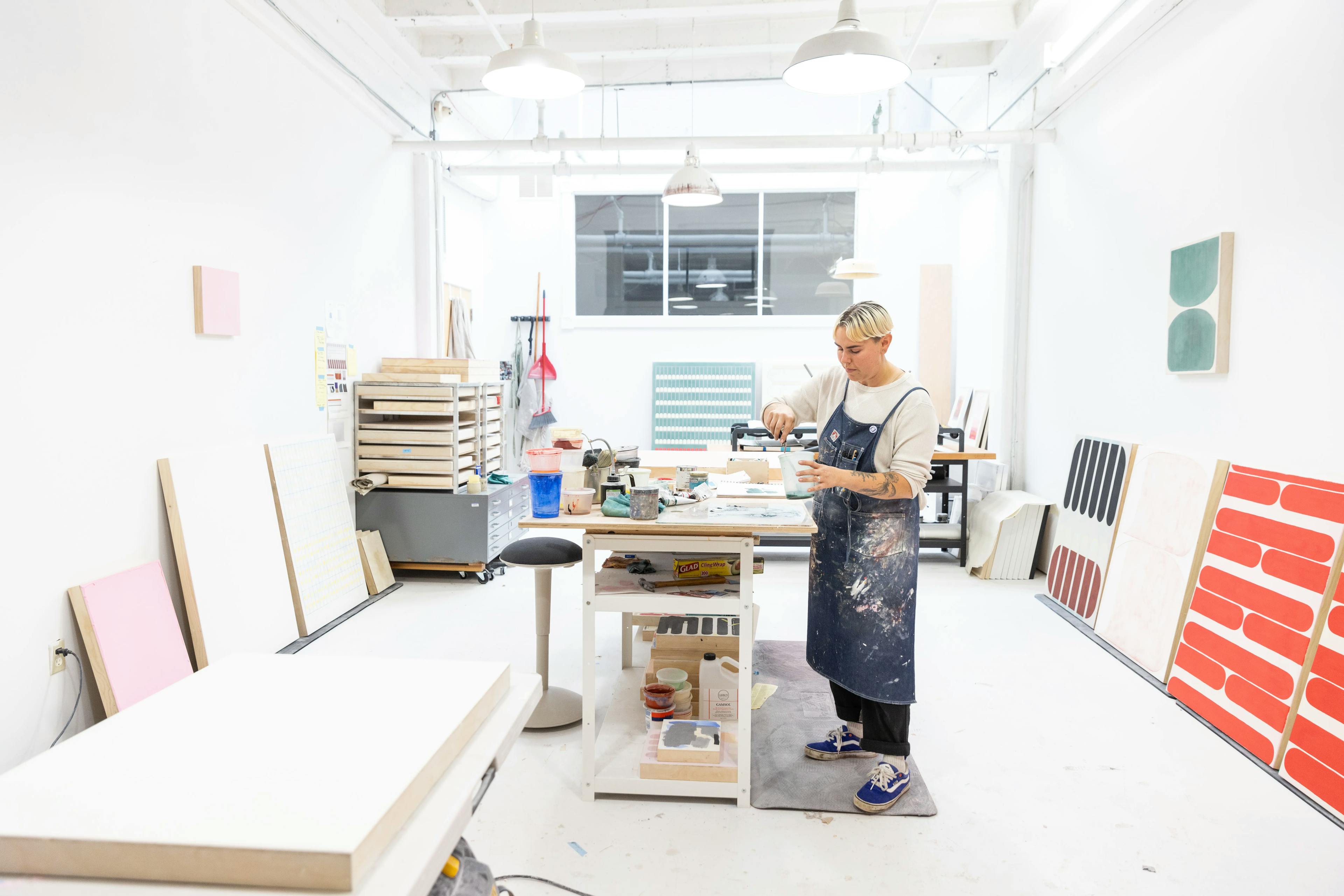 Artist Arielle Zamora working in their studio, surrounded by minimalist, geometric works on panel.