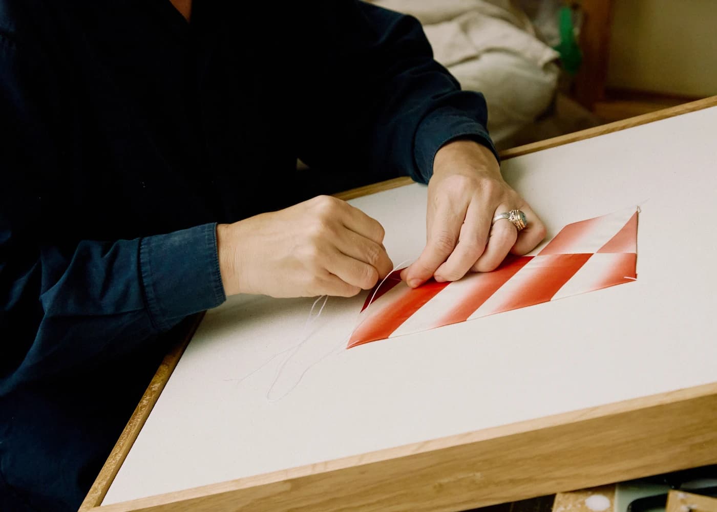 A close-up of artist Mada Vicassiau threading a textile, red and white piece on canvas.