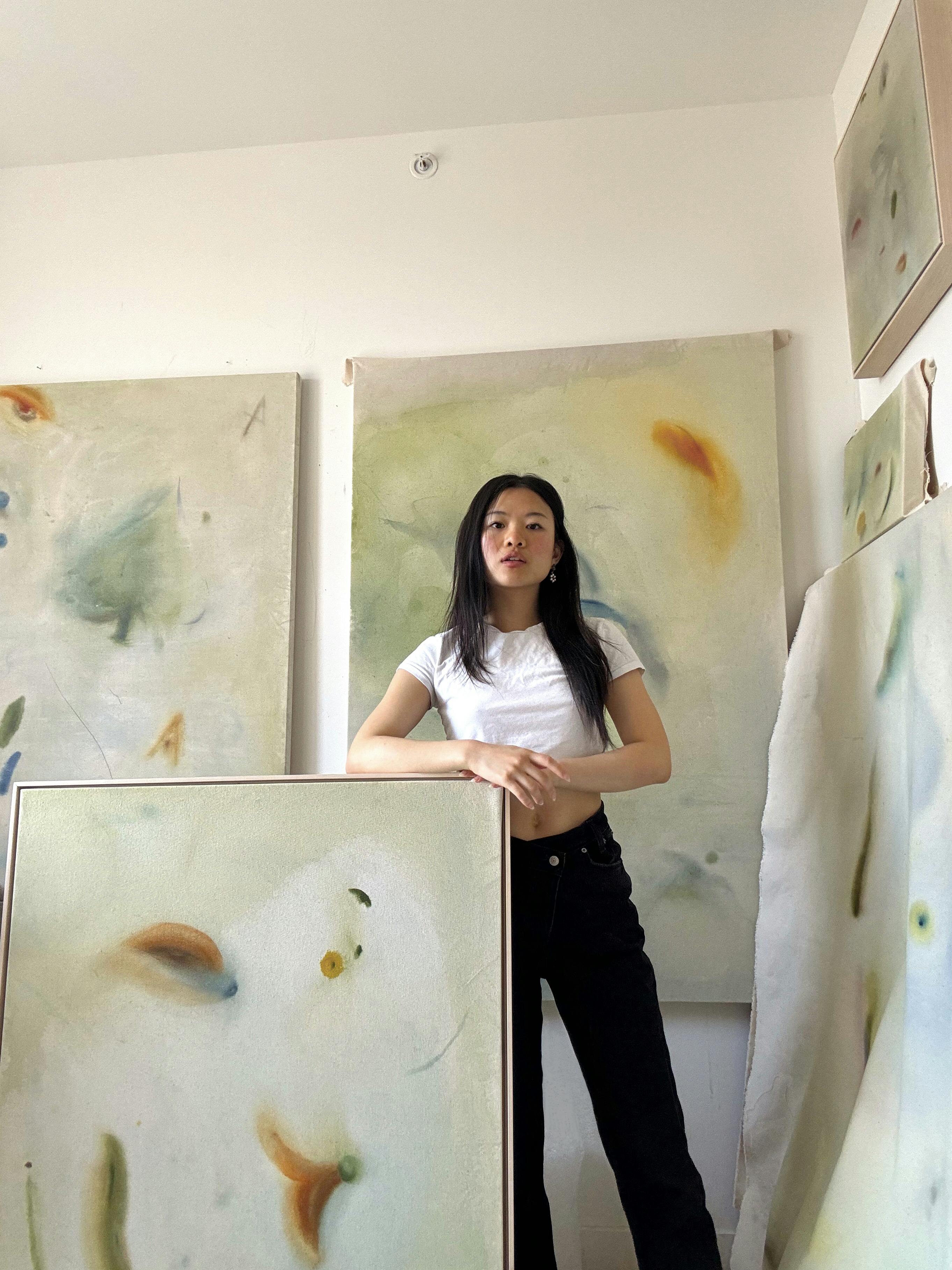 Artist Arlina Cai standing next to a large framed canvas in her studio.
