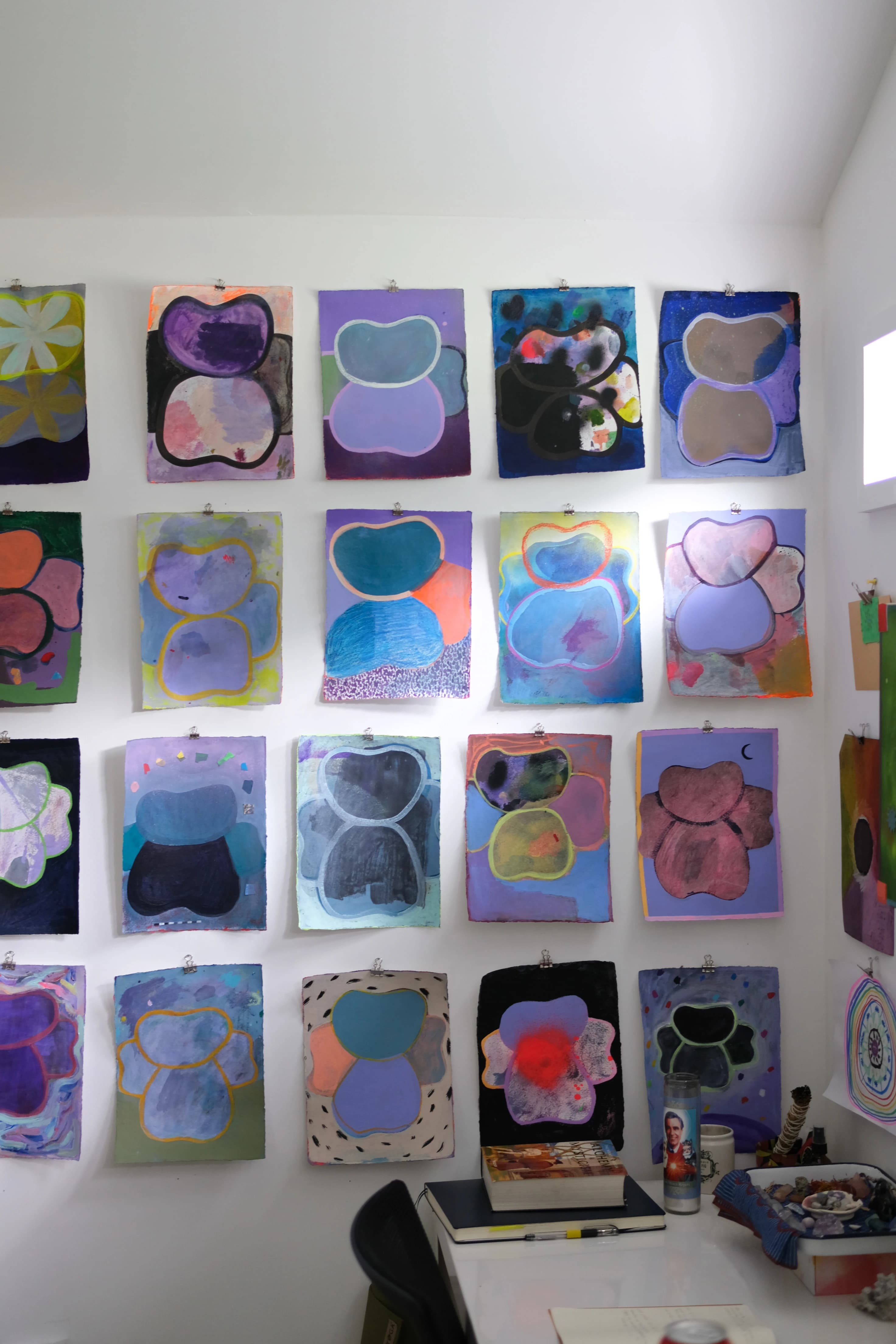 Multiple colorful, abstract works installed on a white wall in artist Ashely Peifer's studio.