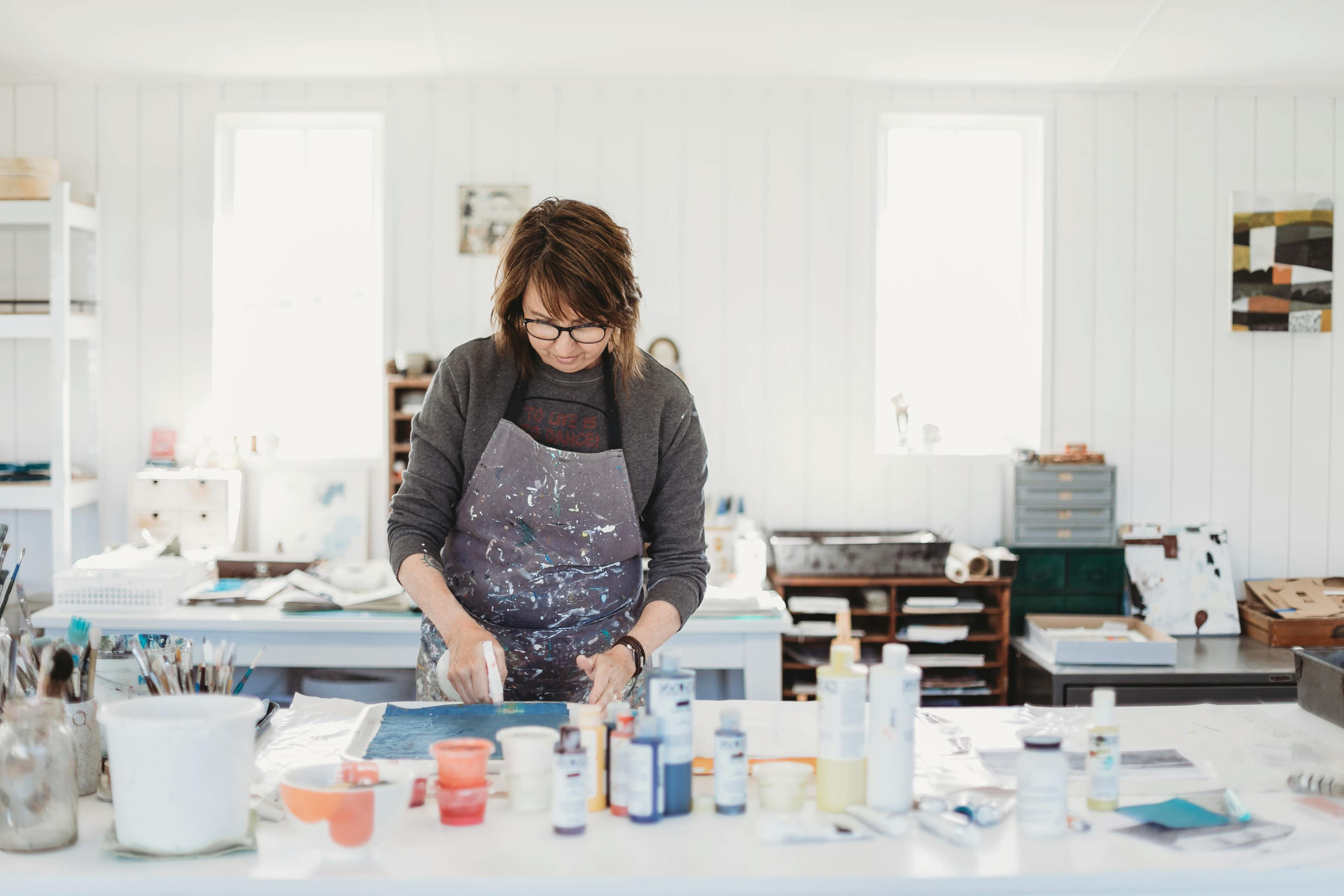Artist Susan Simonini wearing an apron and painting within her white studio.