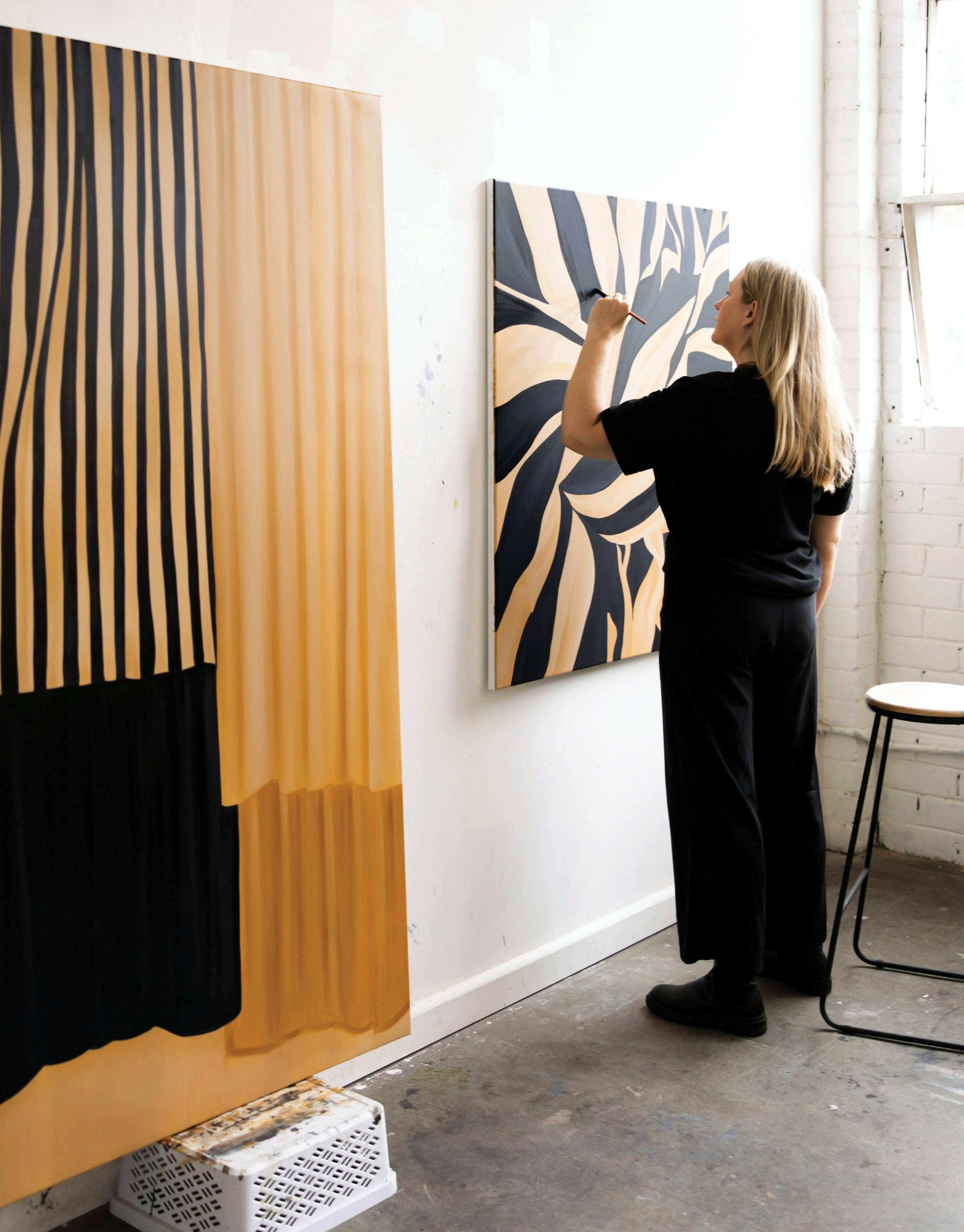 Artist Caroline Walls painting a pattered beige and black work on canvas in her studio.