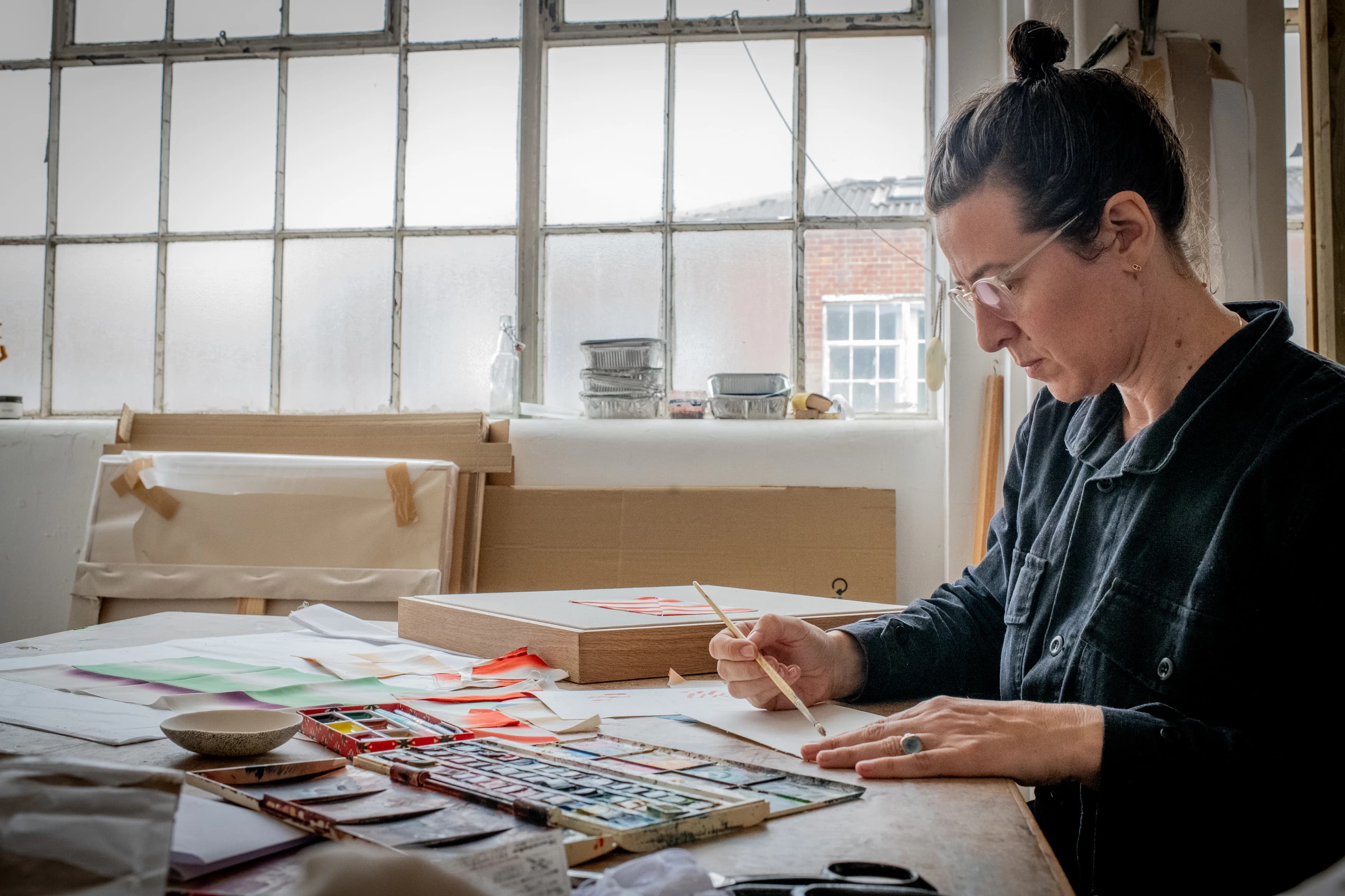 Artist Mada Vicassiau painting with watercolors on paper in her light-filled studio.