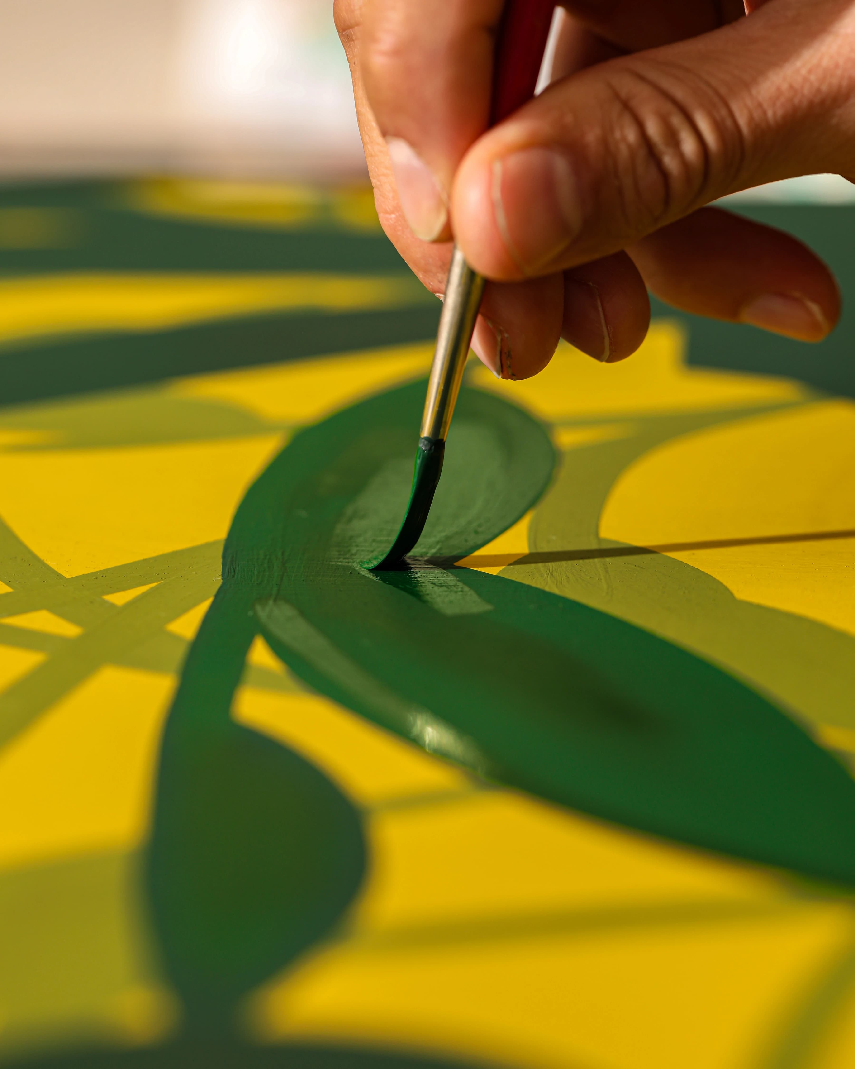 Close-up of artist Eddie Perrote using a thin brush to paint a green line on canvas during his Uprise Art x MacArthur Place Residency.