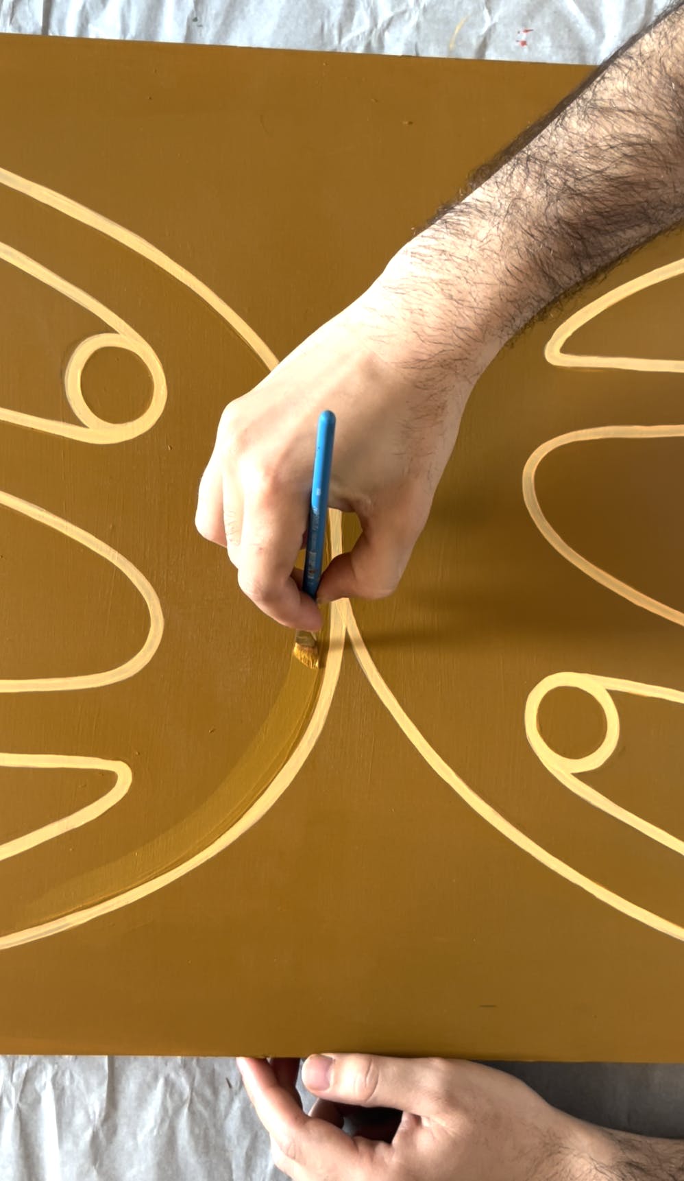 A close-up of artist Lourenço Providência painting intertwined figures on an orange canvas.