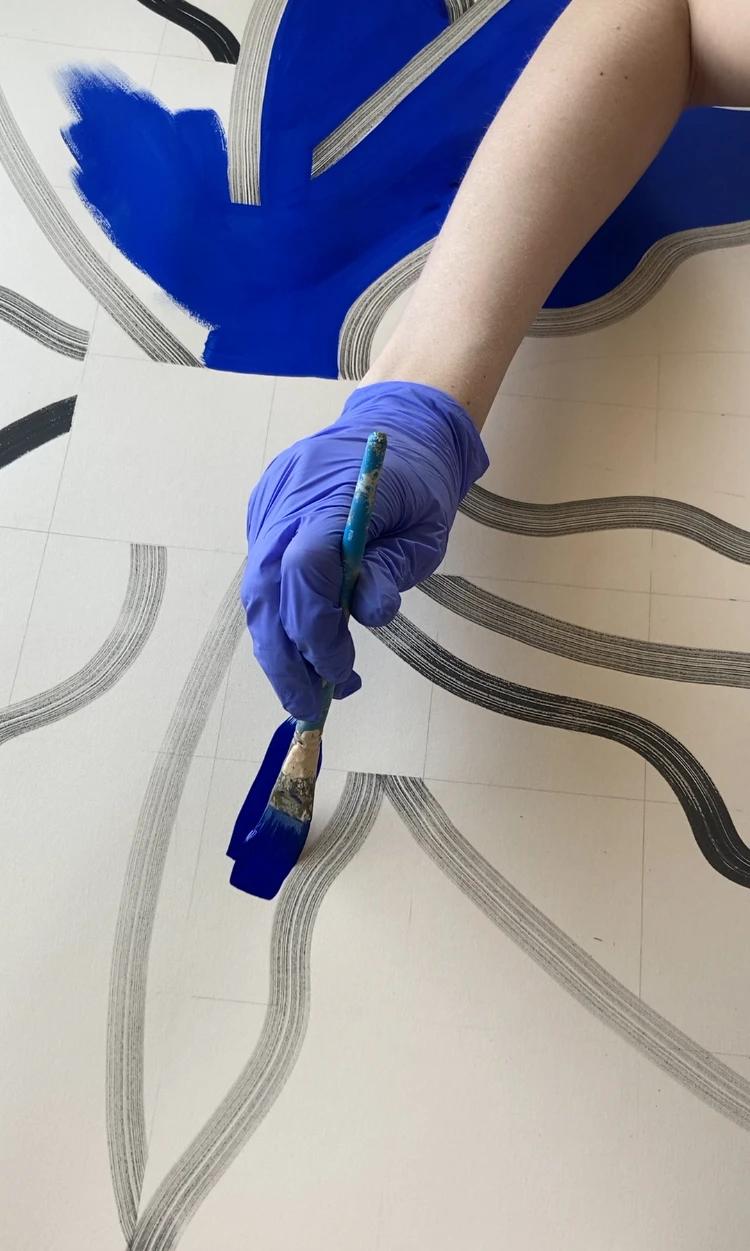 A close-up of artist Anna Koeferl painting swaths of cobalt blue on paper.