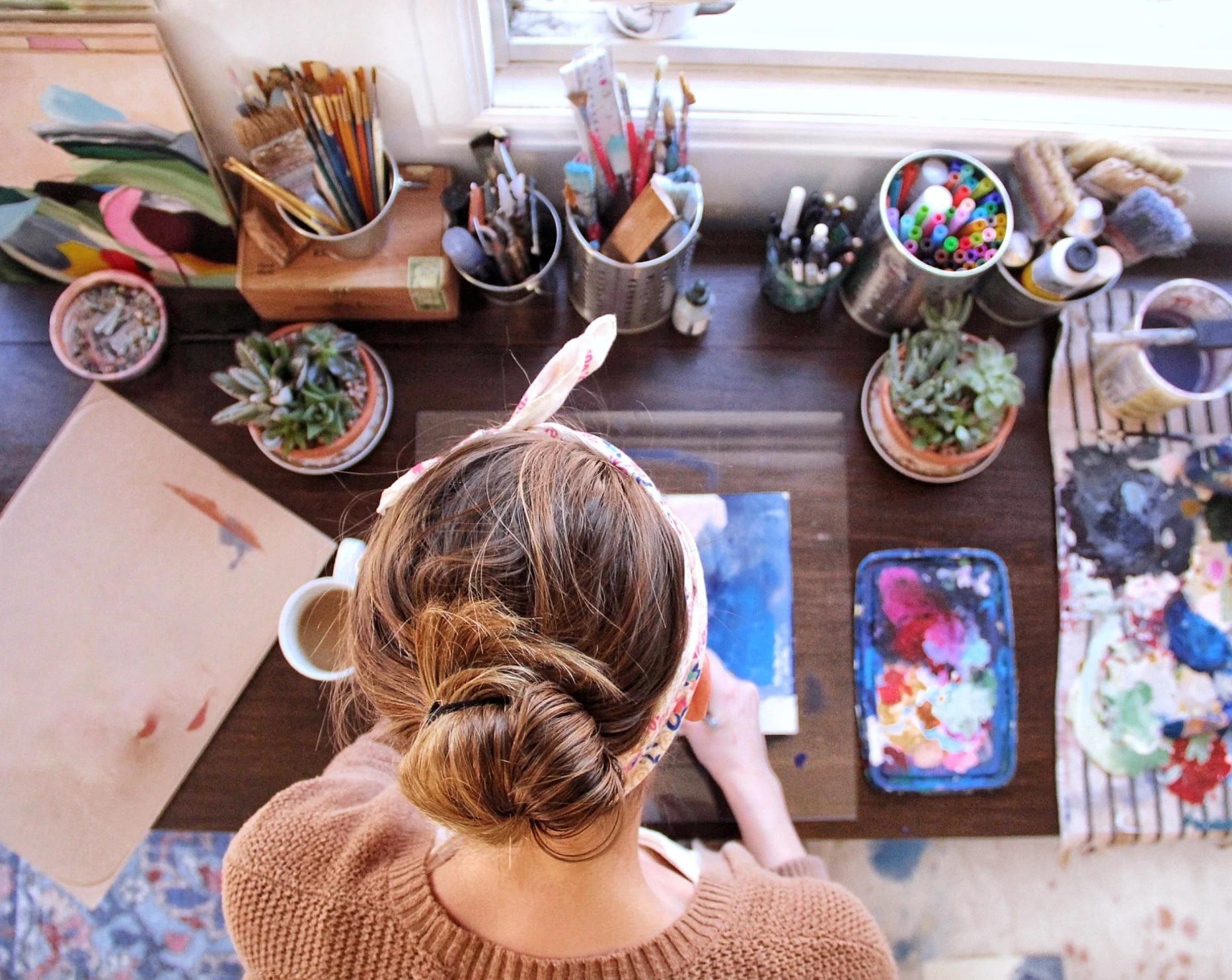 An aerial view of artist Elisa Gomez painting on a table in her studio.