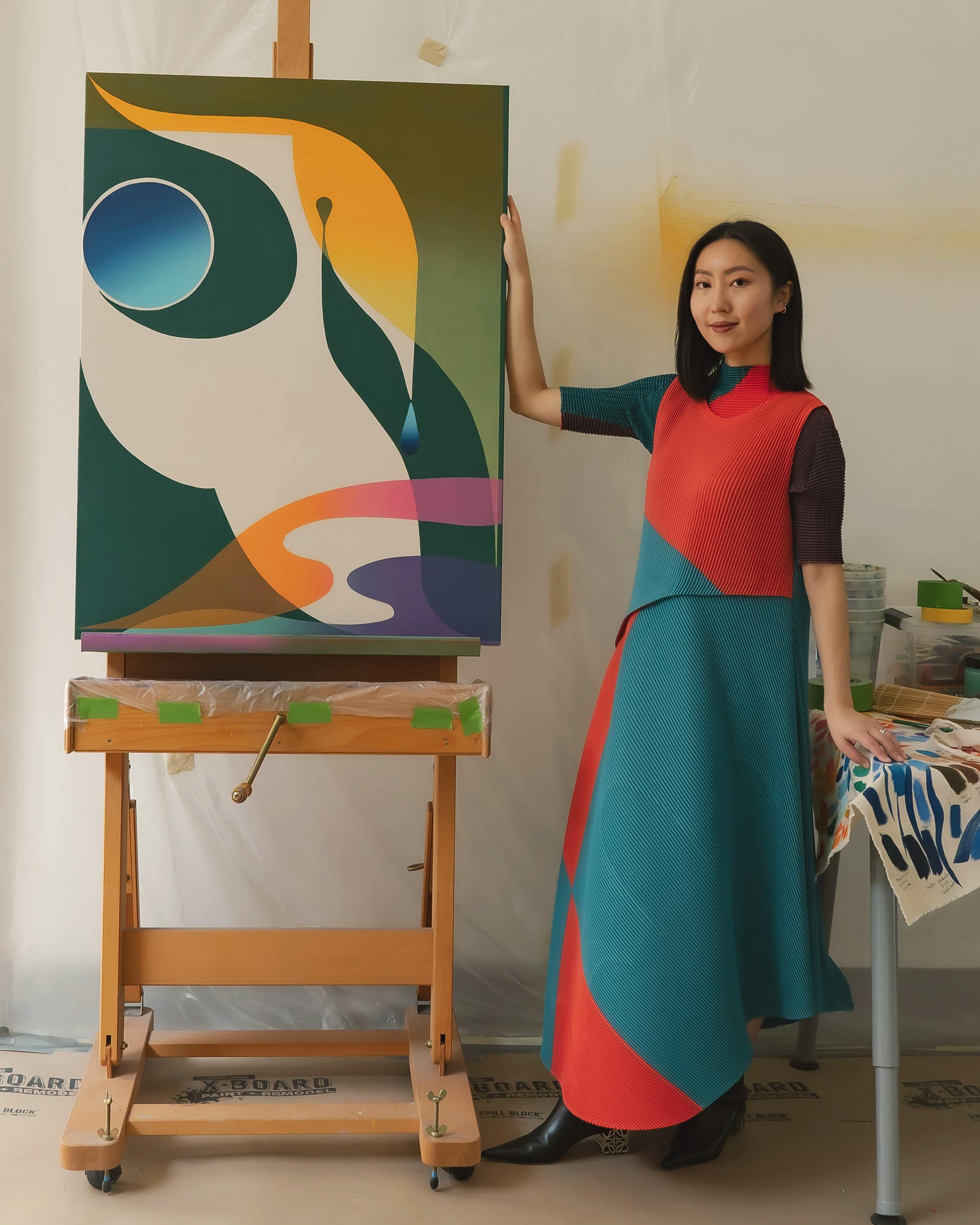 Artist Erin Zhao standing next to a painting on an easel. 