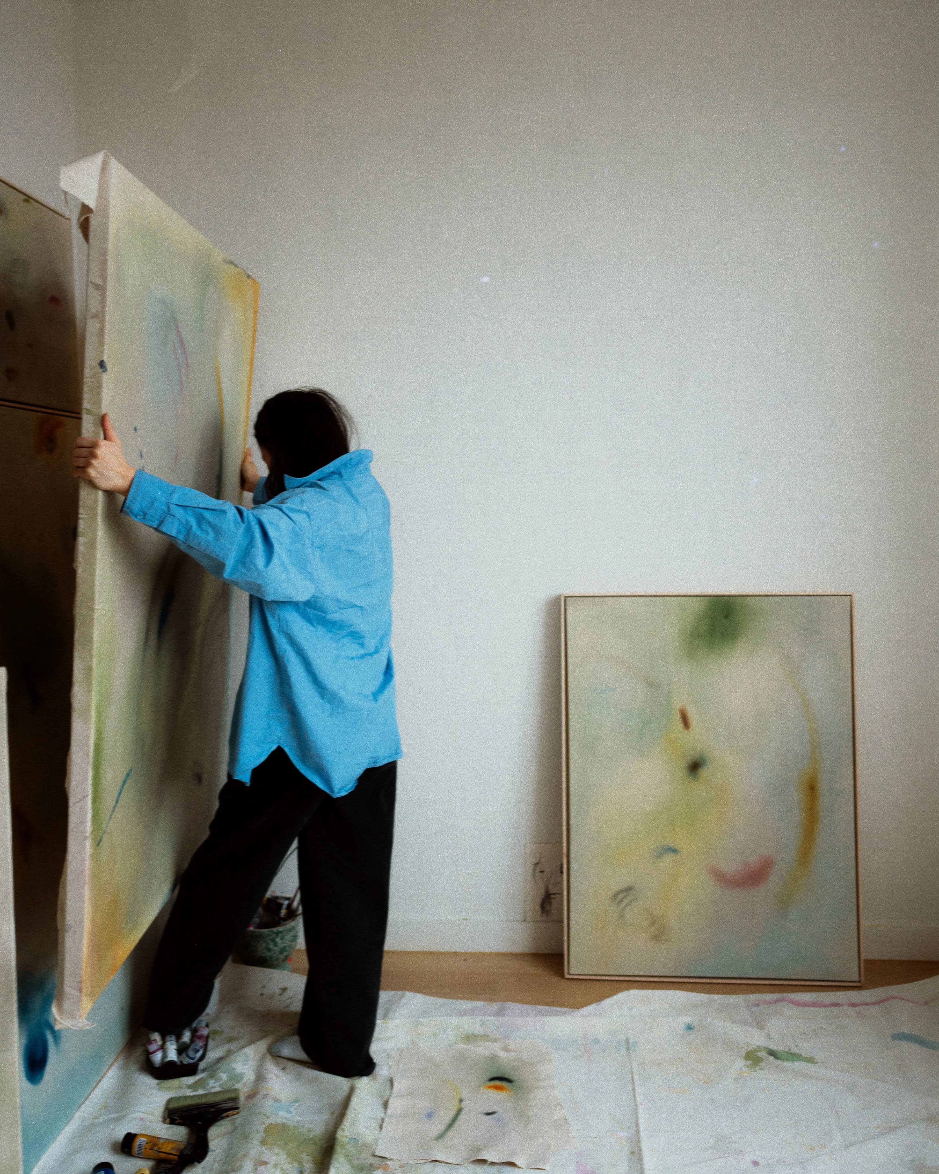 Artist Arlina Cai holding a large canvas work in her studio.