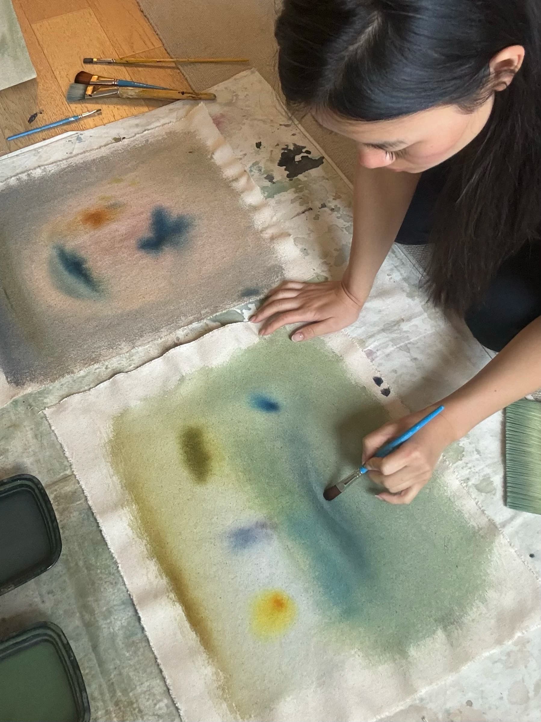 Artist Arlina Cai painting gestural brushstrokes on linen canvas in her studio.