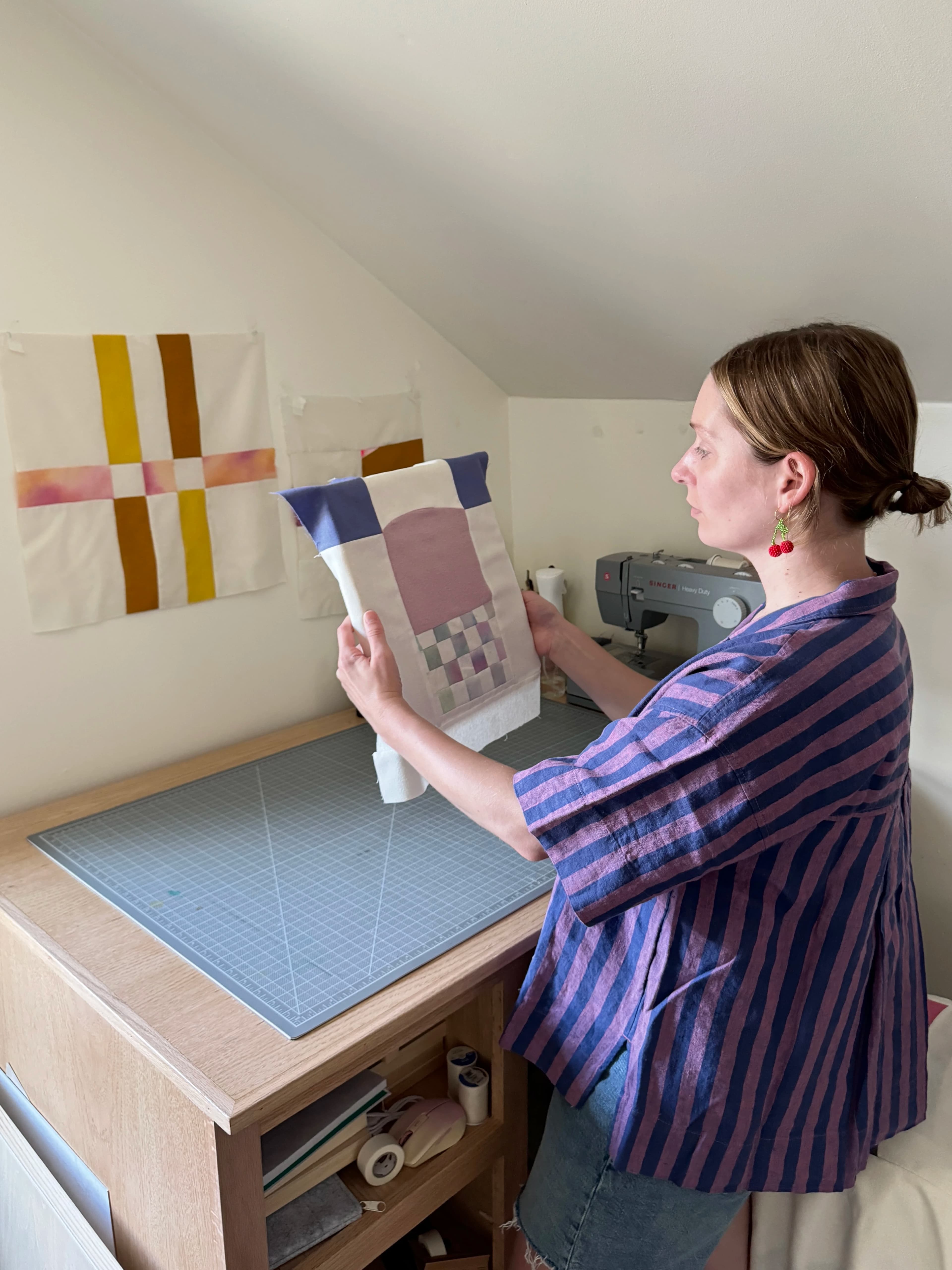 Artist Anastasia Greer holding a small purple textile work in her studio. 