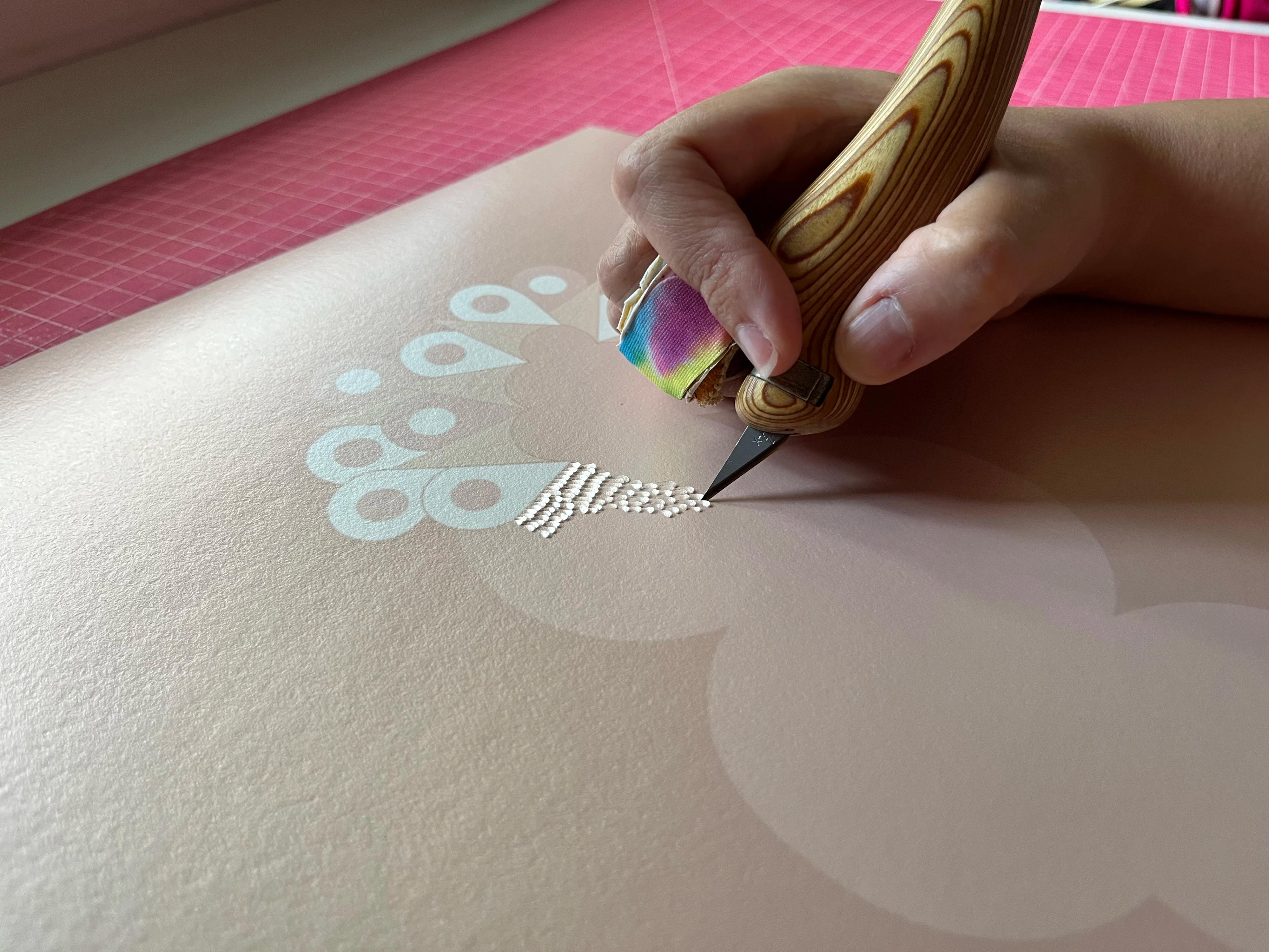 A close-up of artist Lucha Rodríguez cutting into paper with a sharp blade.