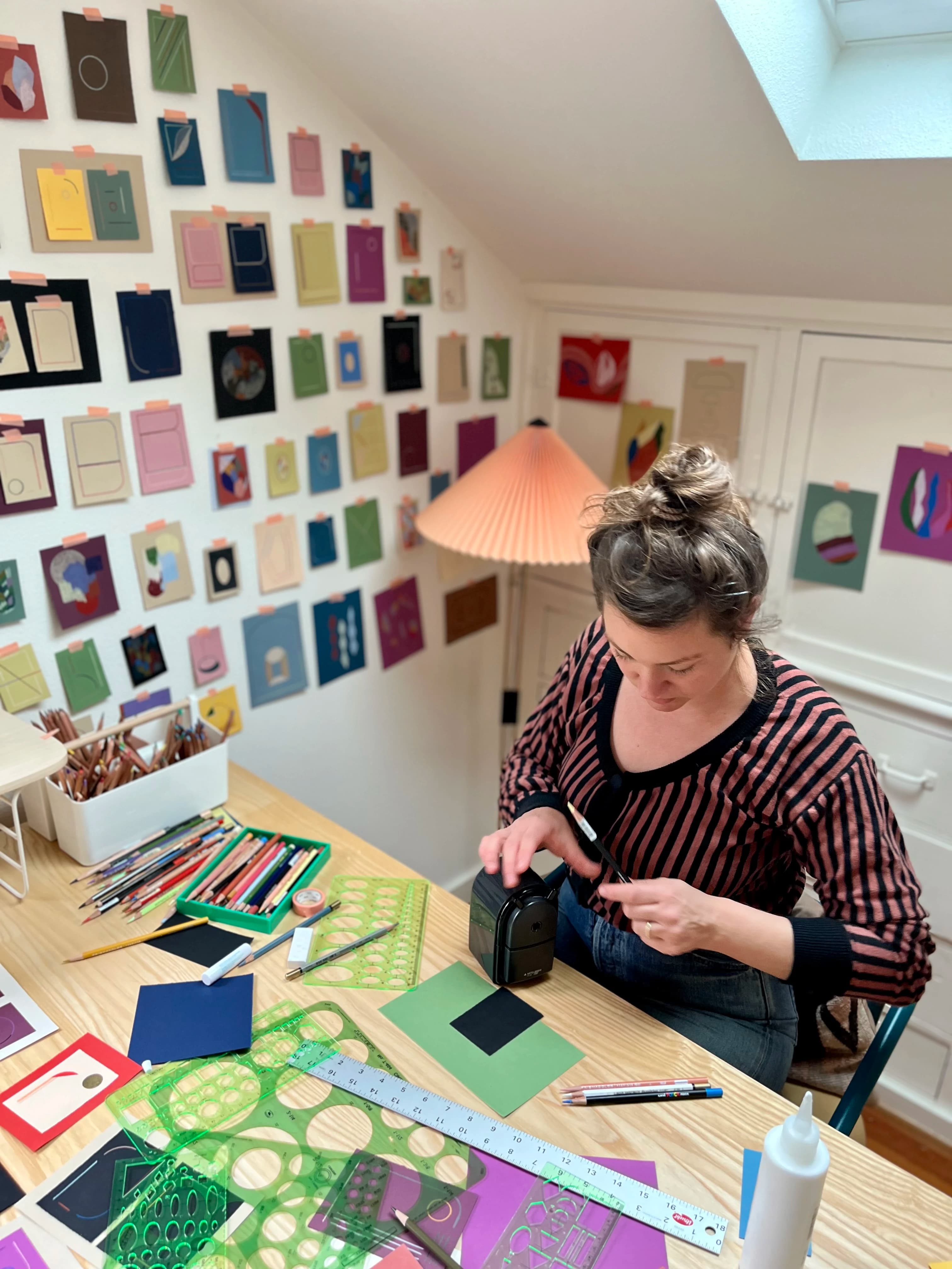 Artist Chloe Fields sitting and working in her studio, surrounded by multiple small works on paper.