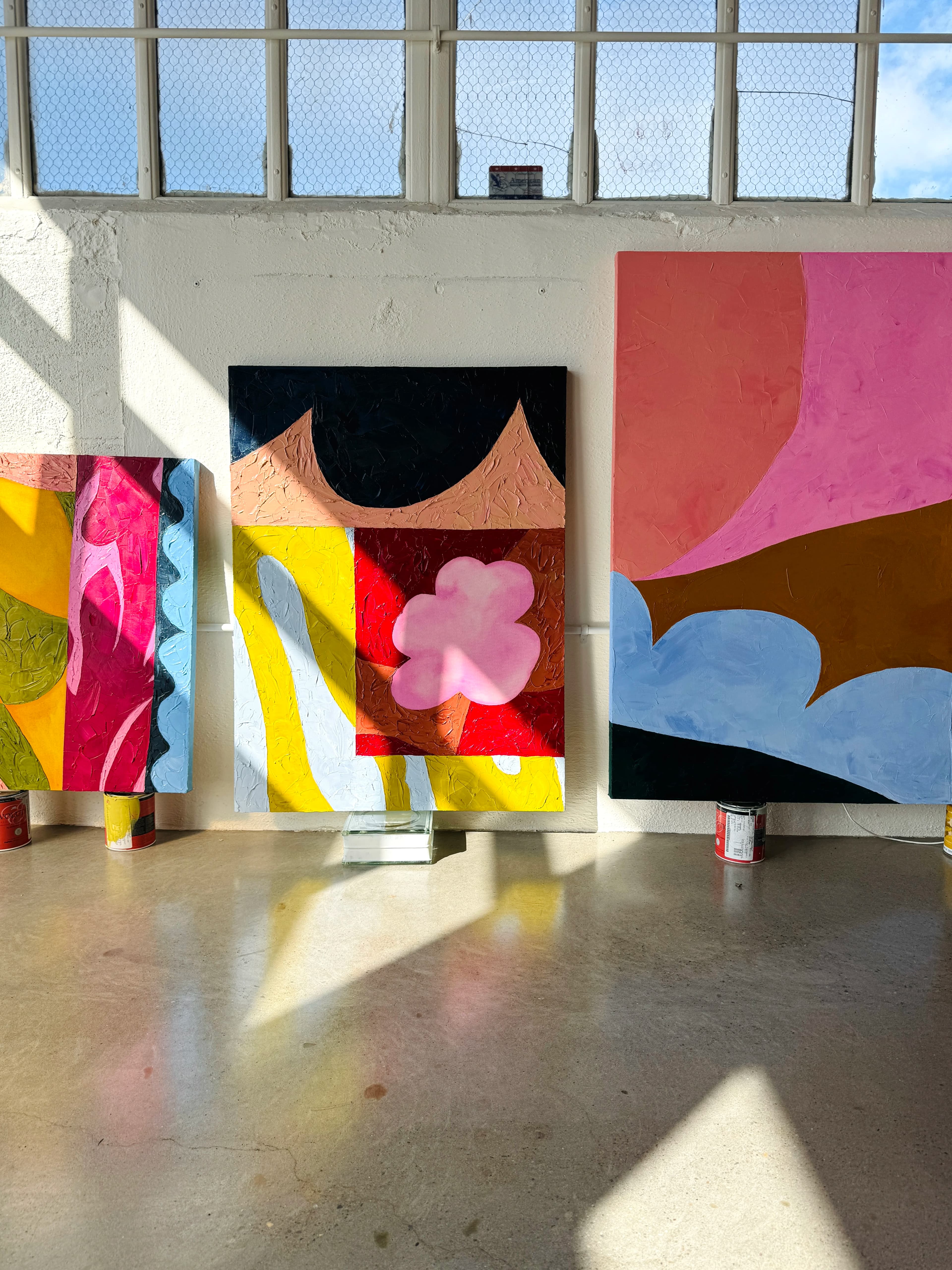 Colorful paintings by artist Alex Proba below a sun-filled window in her studio.