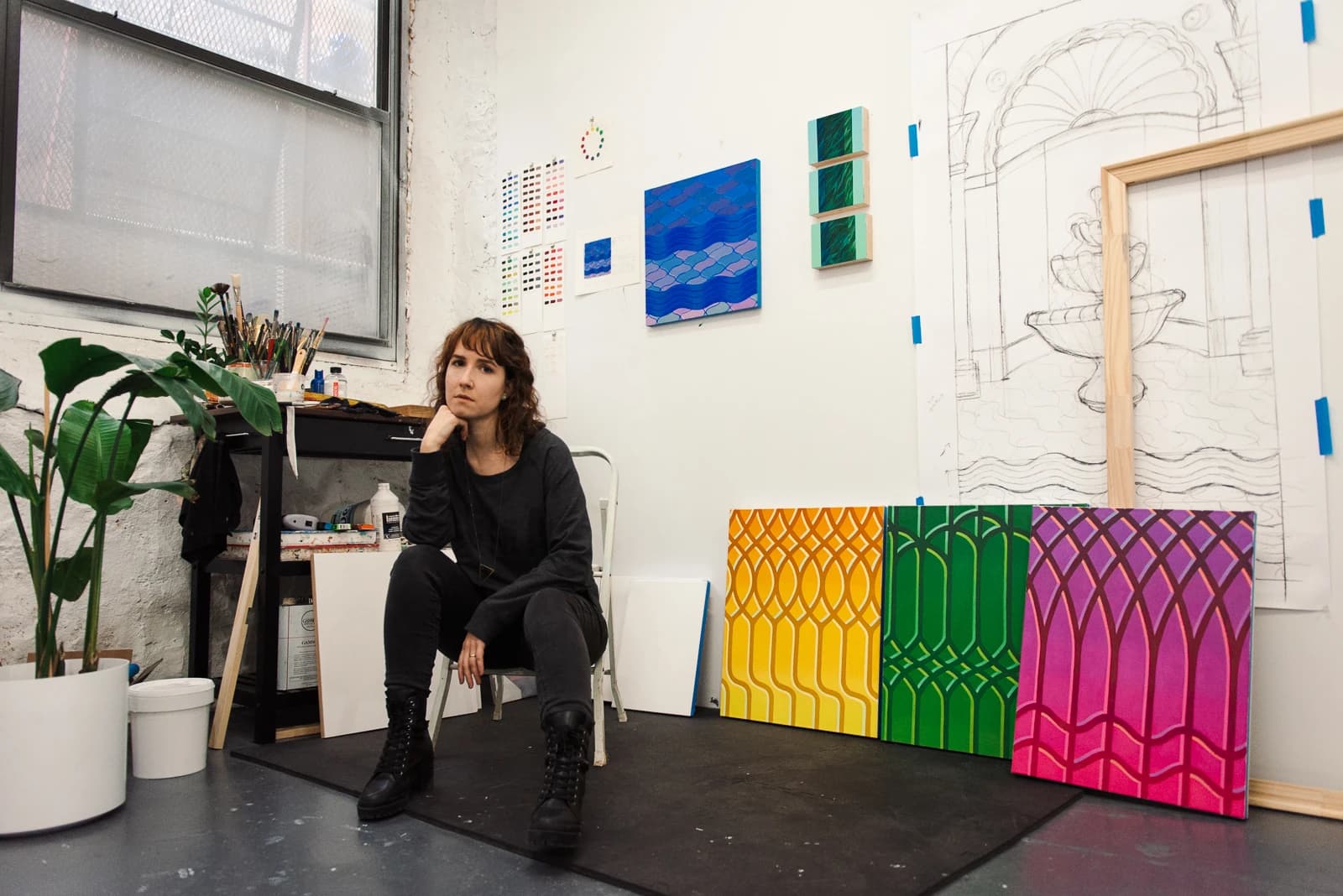 Artist Lucía Rodríguez Pérez sitting on a chair in her studio, surrounded by her works and sketches.