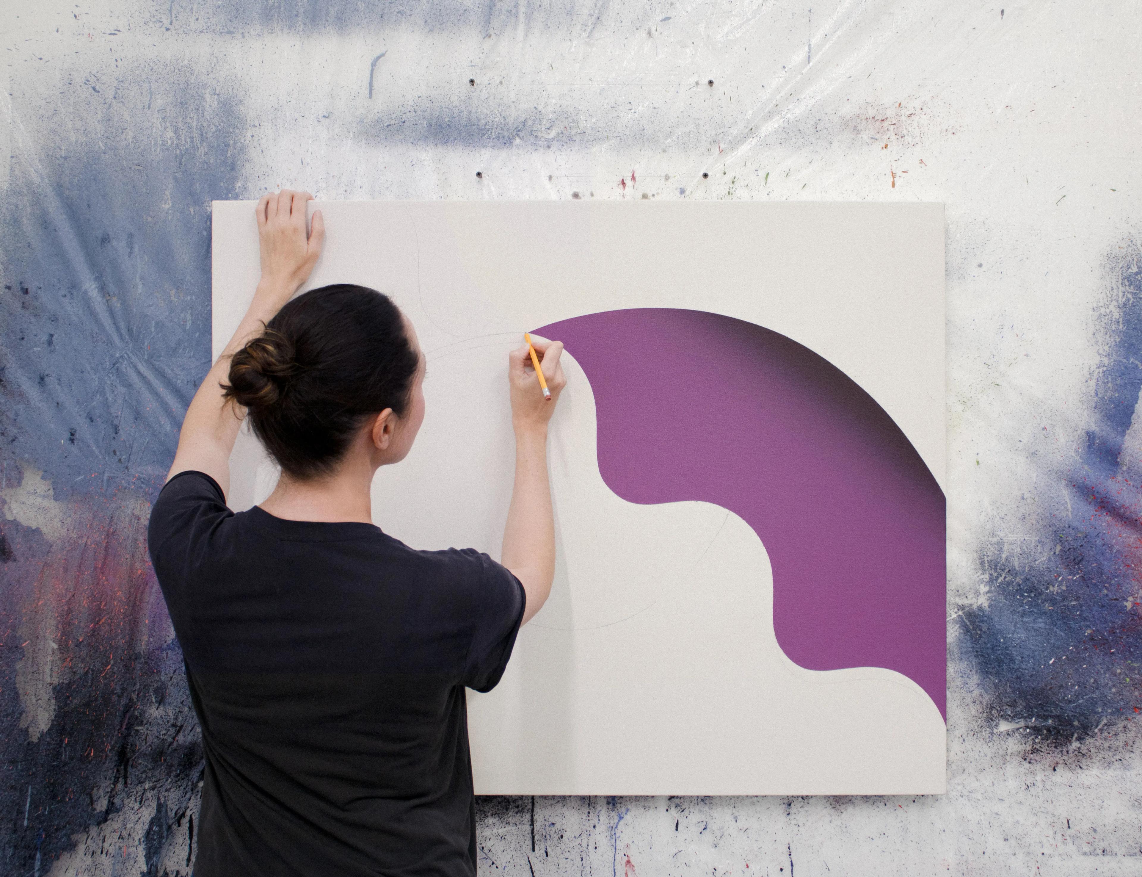 Artist Senem Oezdogan painting a purple shape on a beige canvas in her studio.