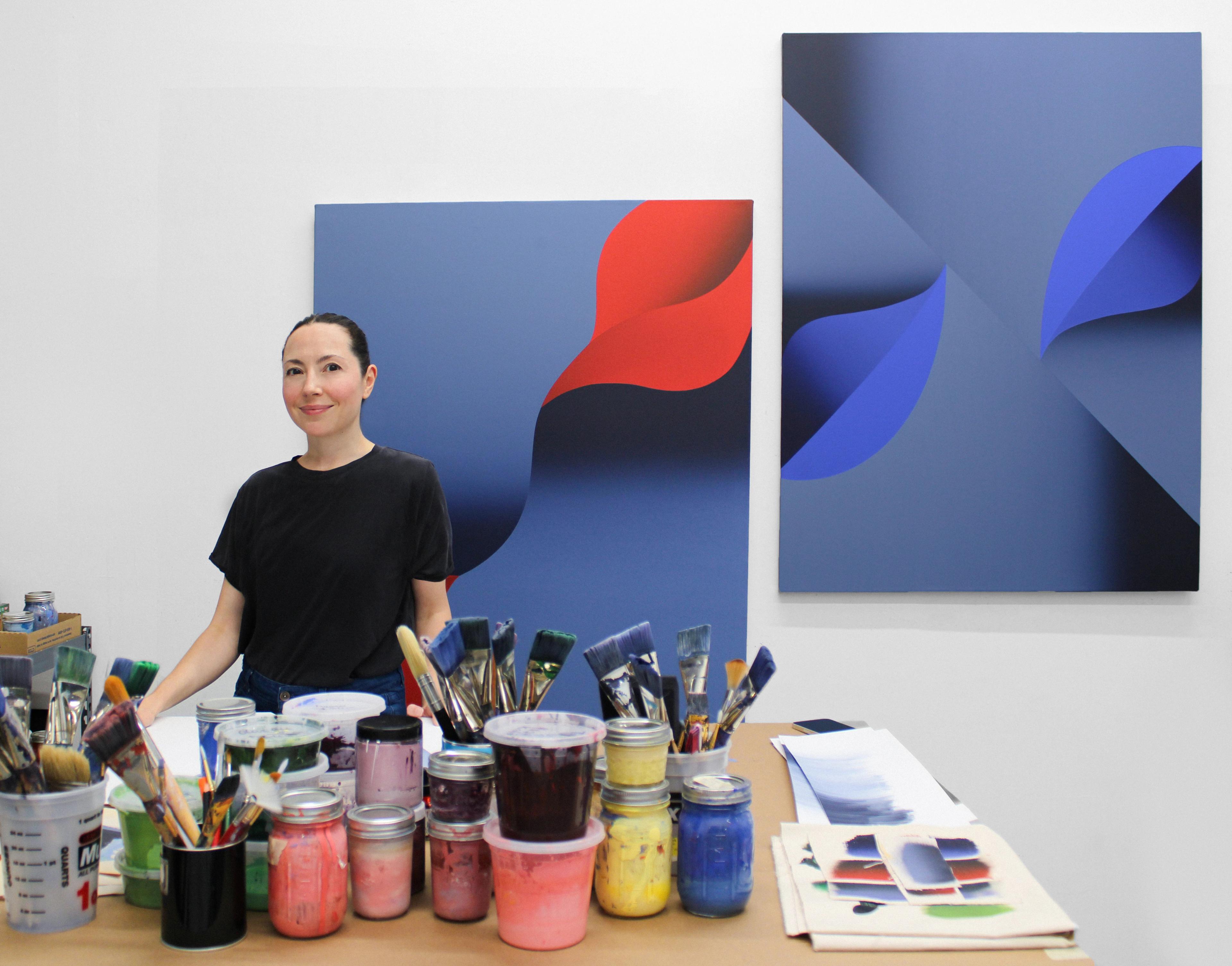 Artist Senem Oezdogan standing in her studio in front of two, blue minimalist compositions.