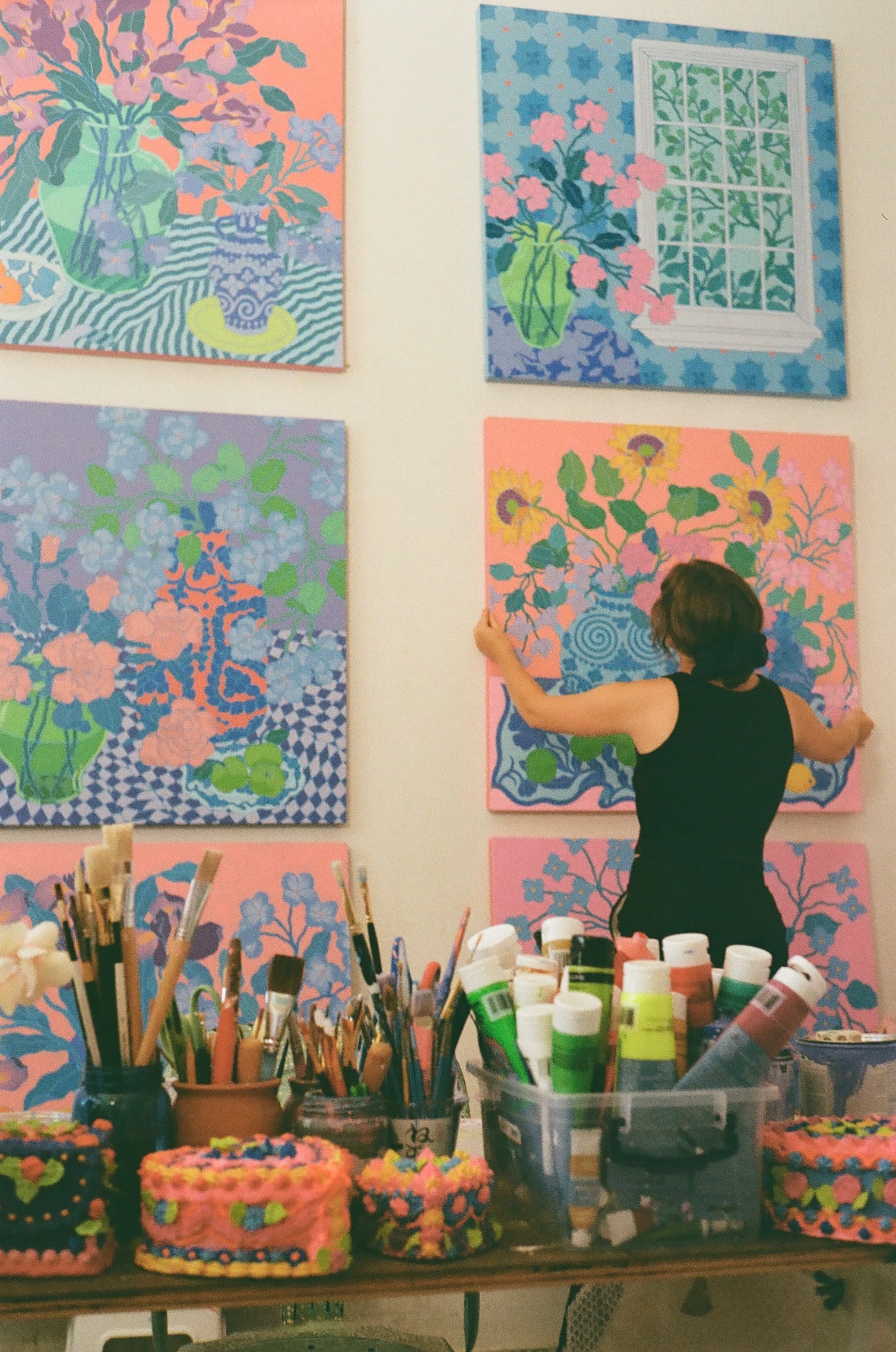 Artist Sarah Ingraham holding a floral still life painting in her studio.