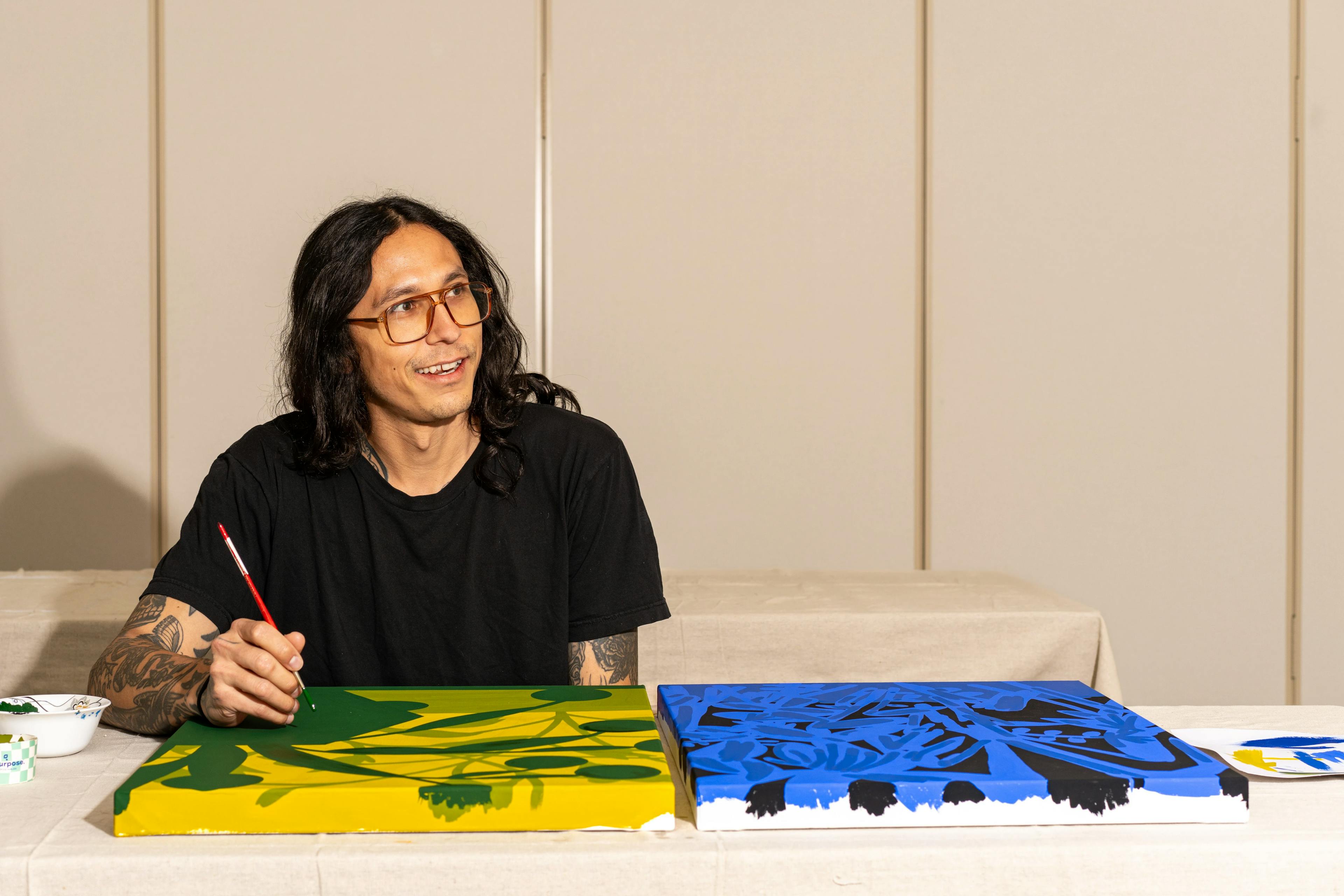 Artist Eddie Perrote painting two canvases, one yellow and one blue, within a studio as part of his Uprise Art x MacArthur Place Residency.