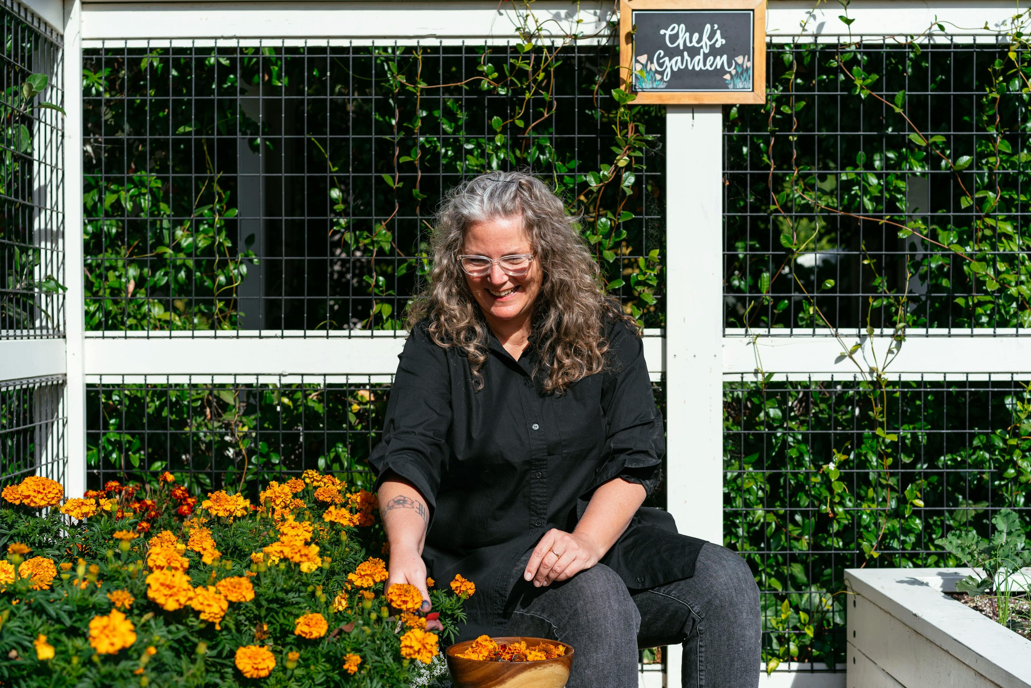 Artist Carrie Crawford picking orange flowers in a garden at MacArthur Place.