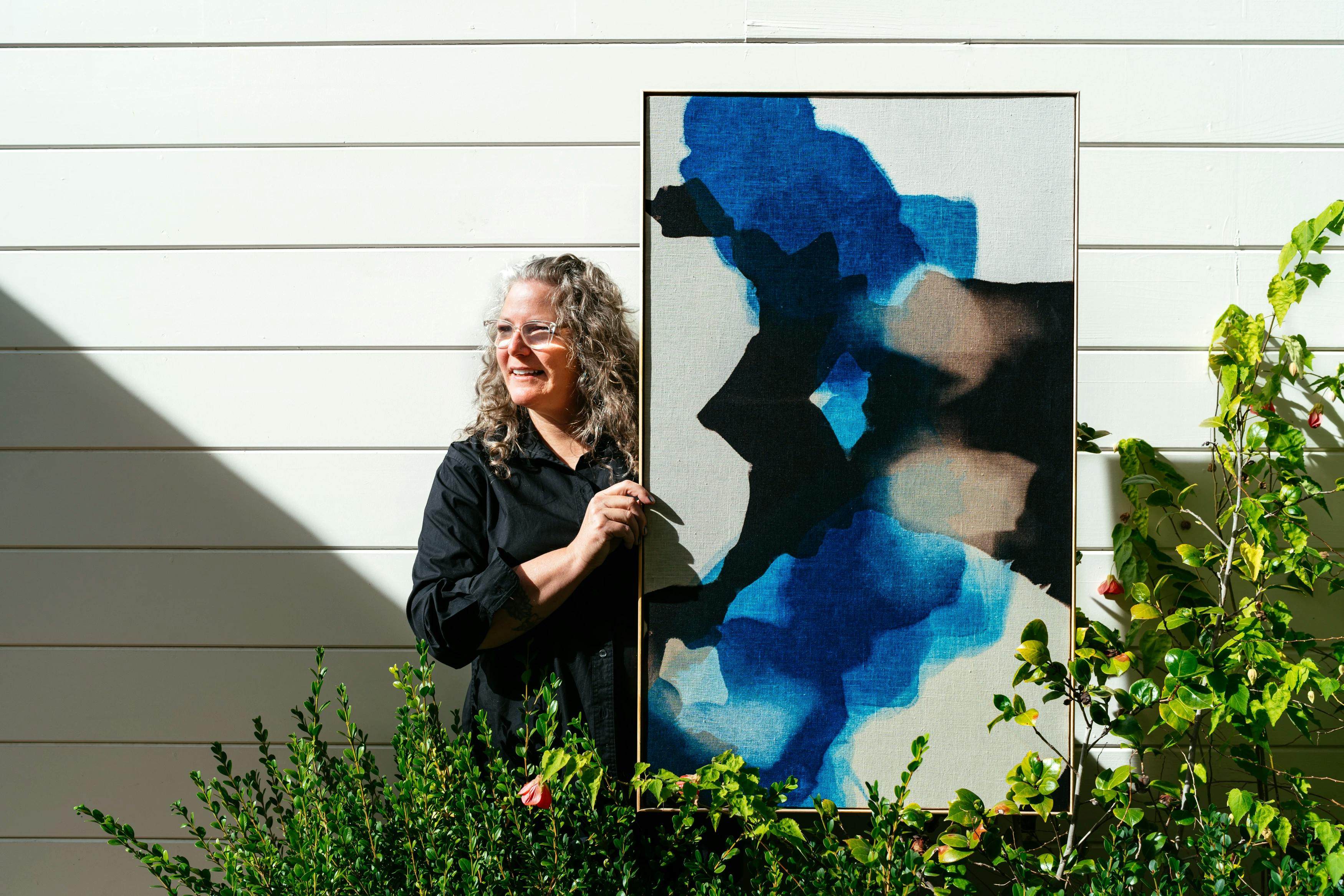 Artist Carrie Crawford holding up a naturally-dyed indigo and white artwork at MacArthur Place.