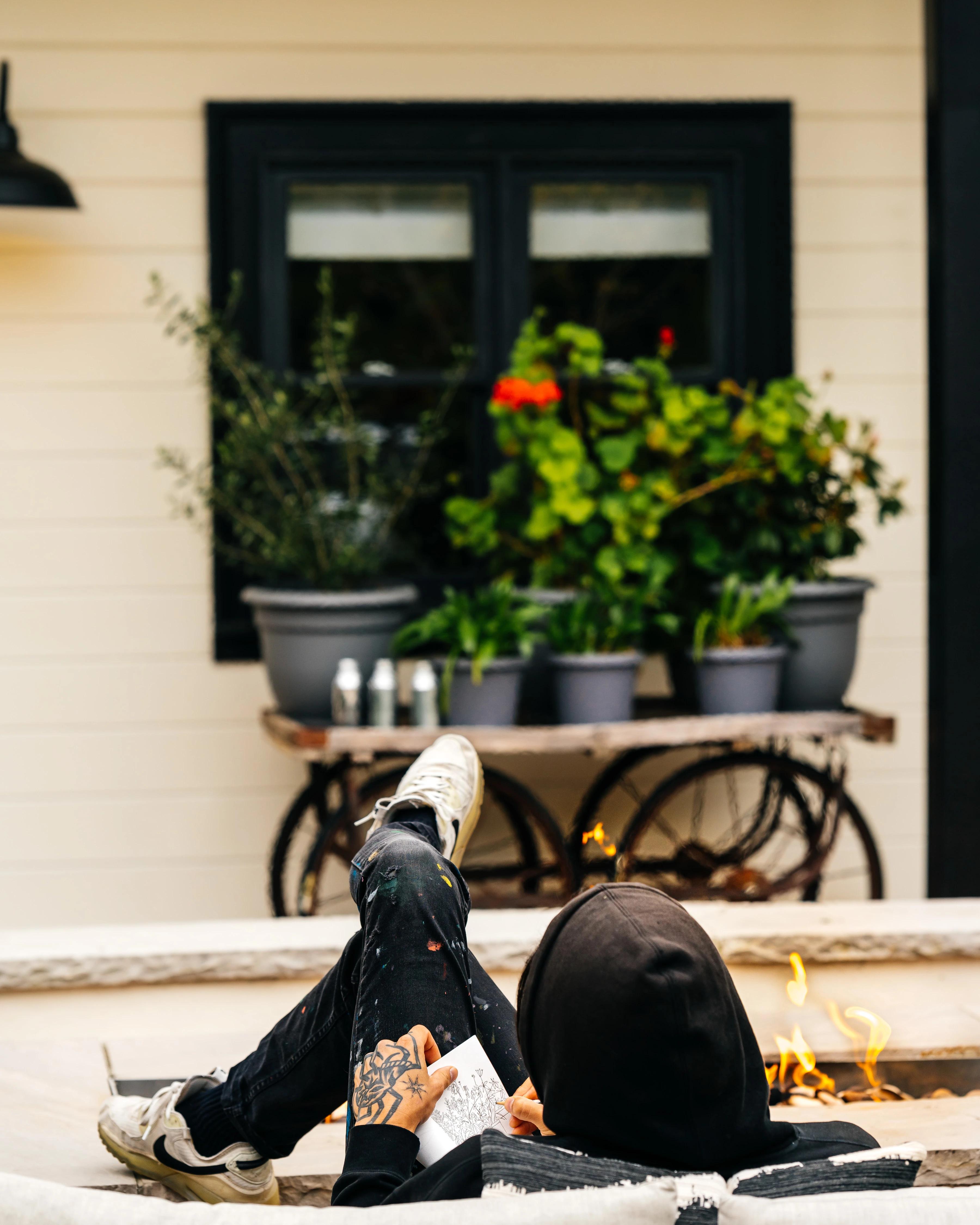 Artist Eddie Perrote sketching in a small notebook sitting next to an outdoor fire pit during his Uprise Art x MacArthur Place Residency.