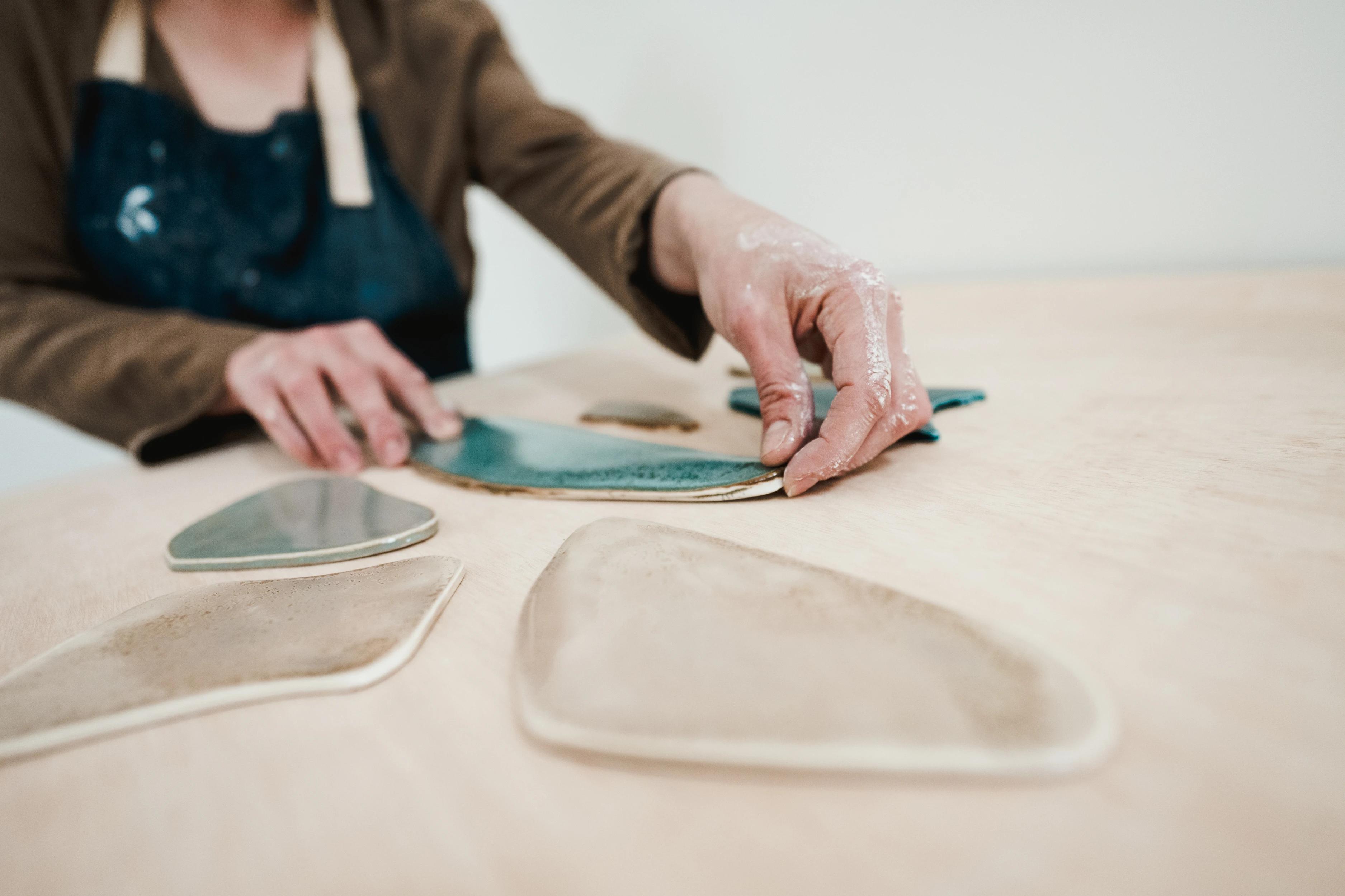 A close-up of artist Christina Watka placing glazed porcelain pieces on a wooden table.