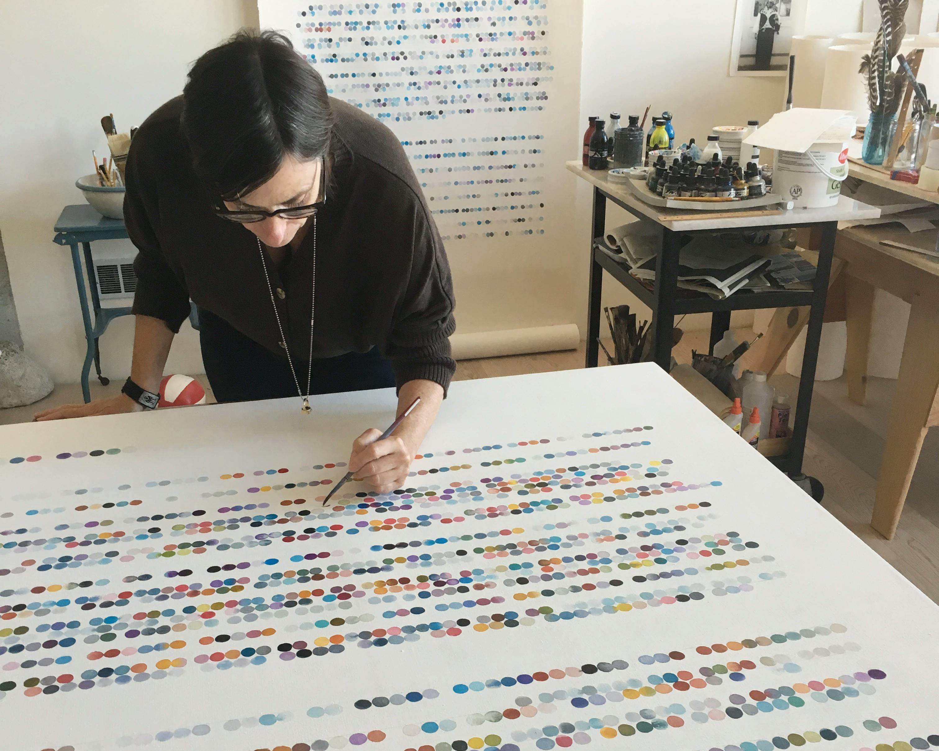 Artist Gail Tarantino working on a large, text-based work with concentric circles in her studio.