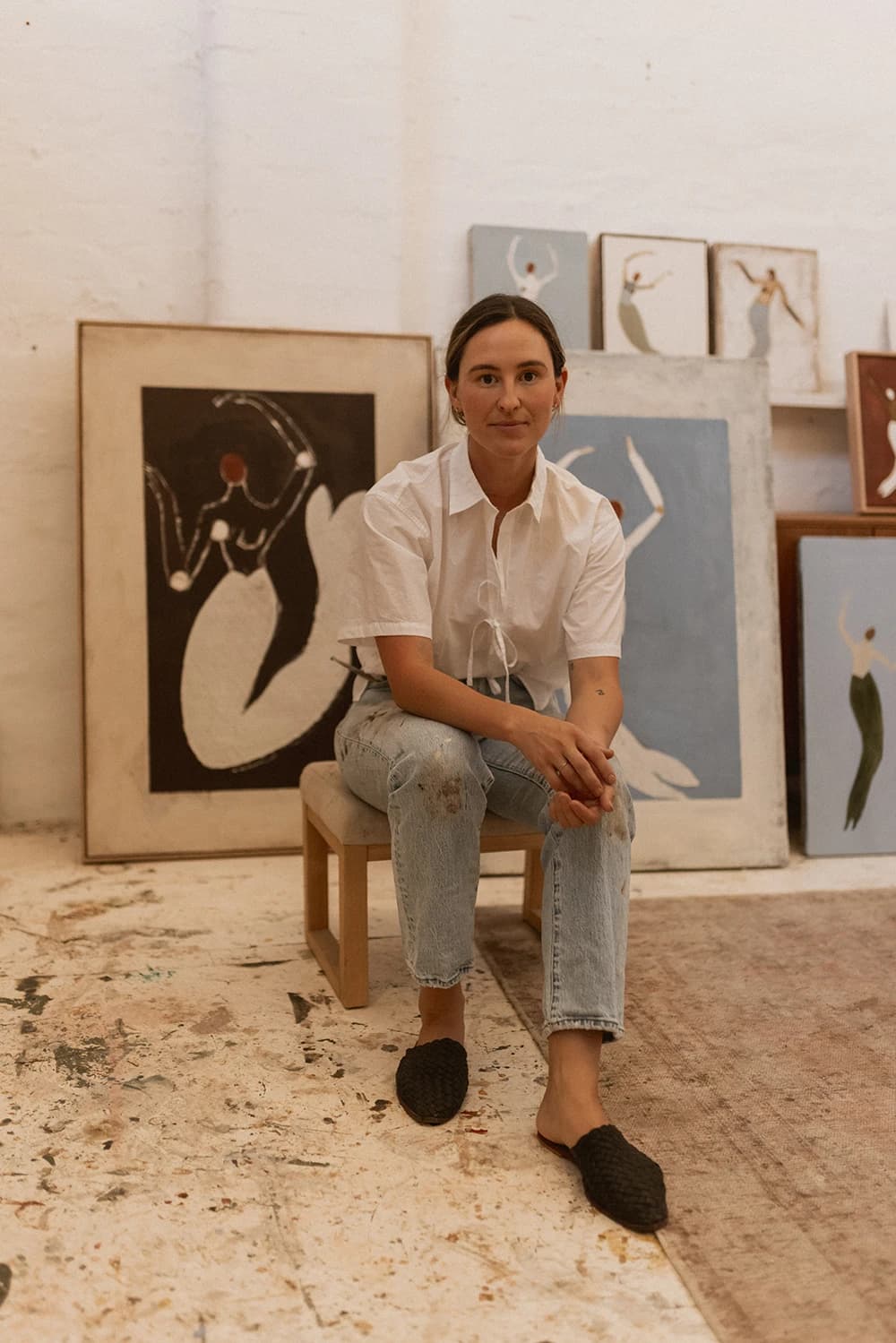 Artist Brittany Ferns sitting in her studio surrounded by her mythology-inspired paintings.