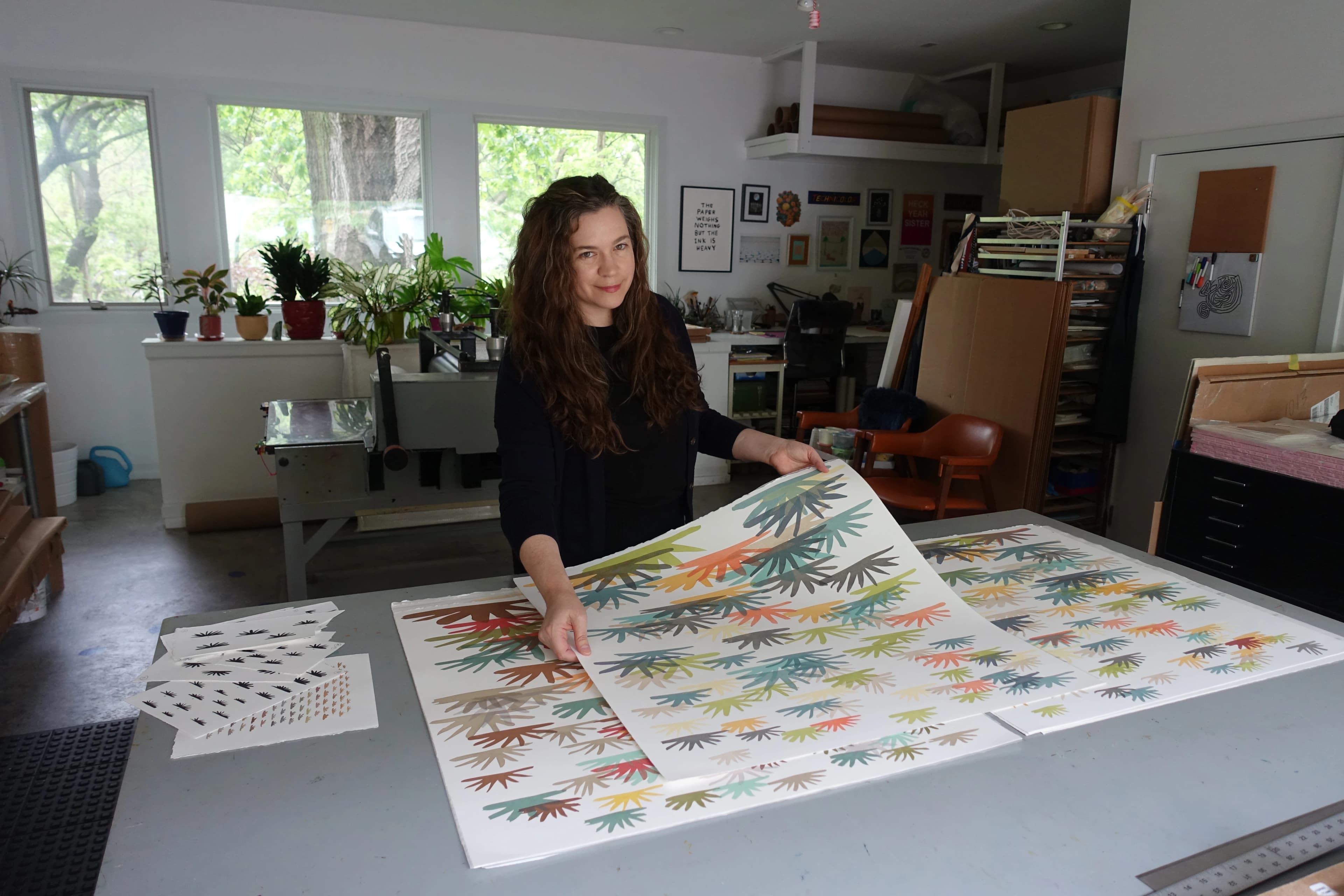 Artist Laura Berman holding large, colorful collages in her studio.