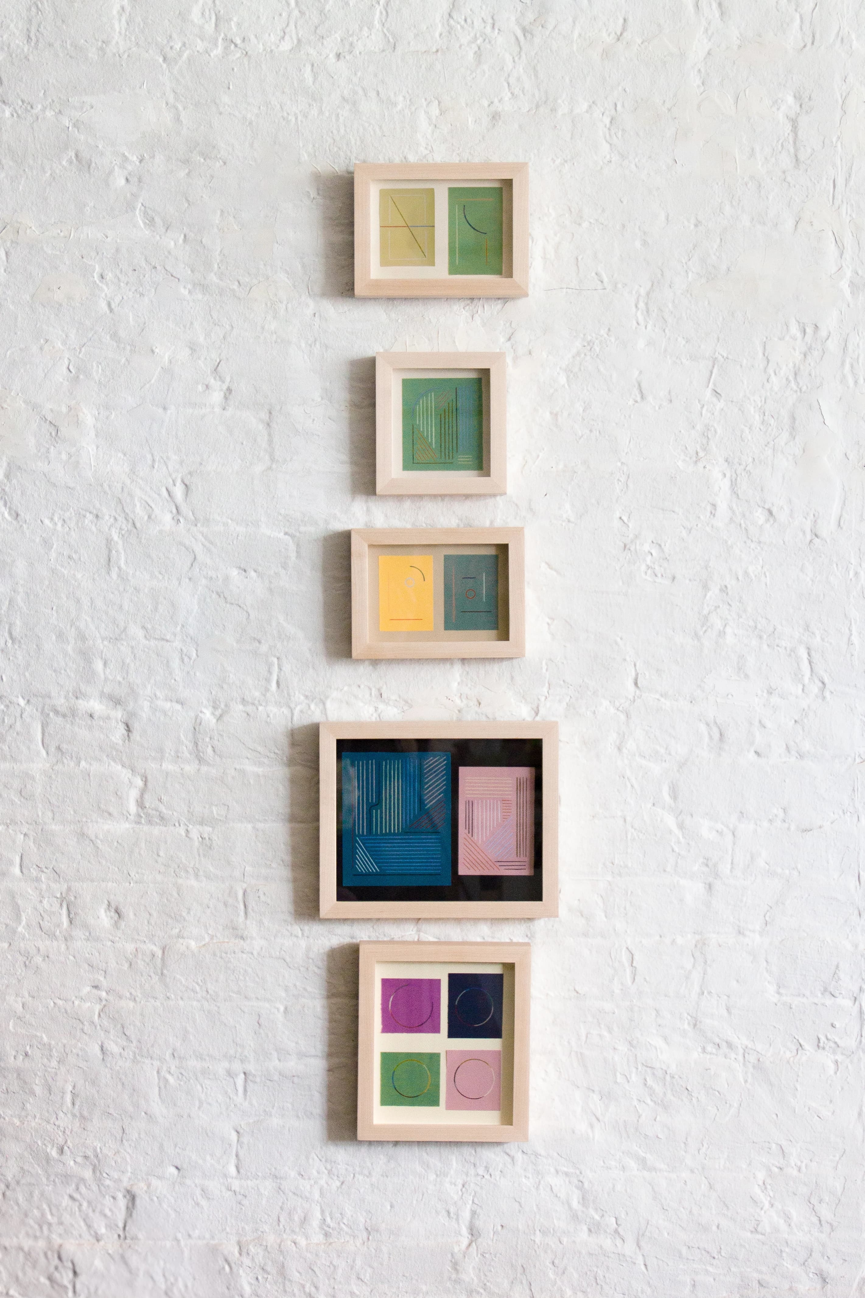 A totem of small, framed works on paper by artist Chloe Fields installed on a white wall at Uprise Art.