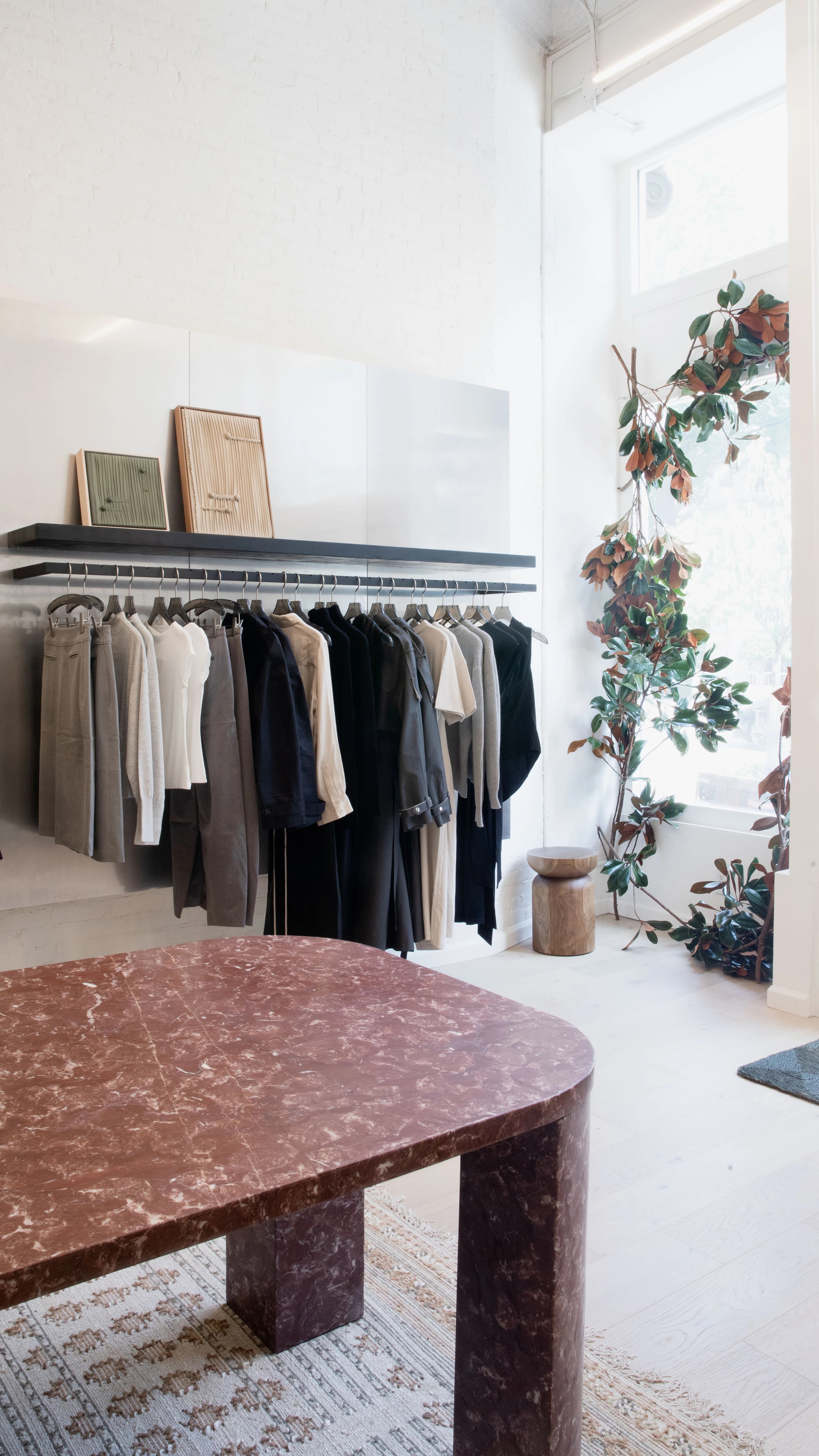 Artworks by Nicole Anastas lean on a shelf above a rack of clothes at Modern Citizen's New York store.