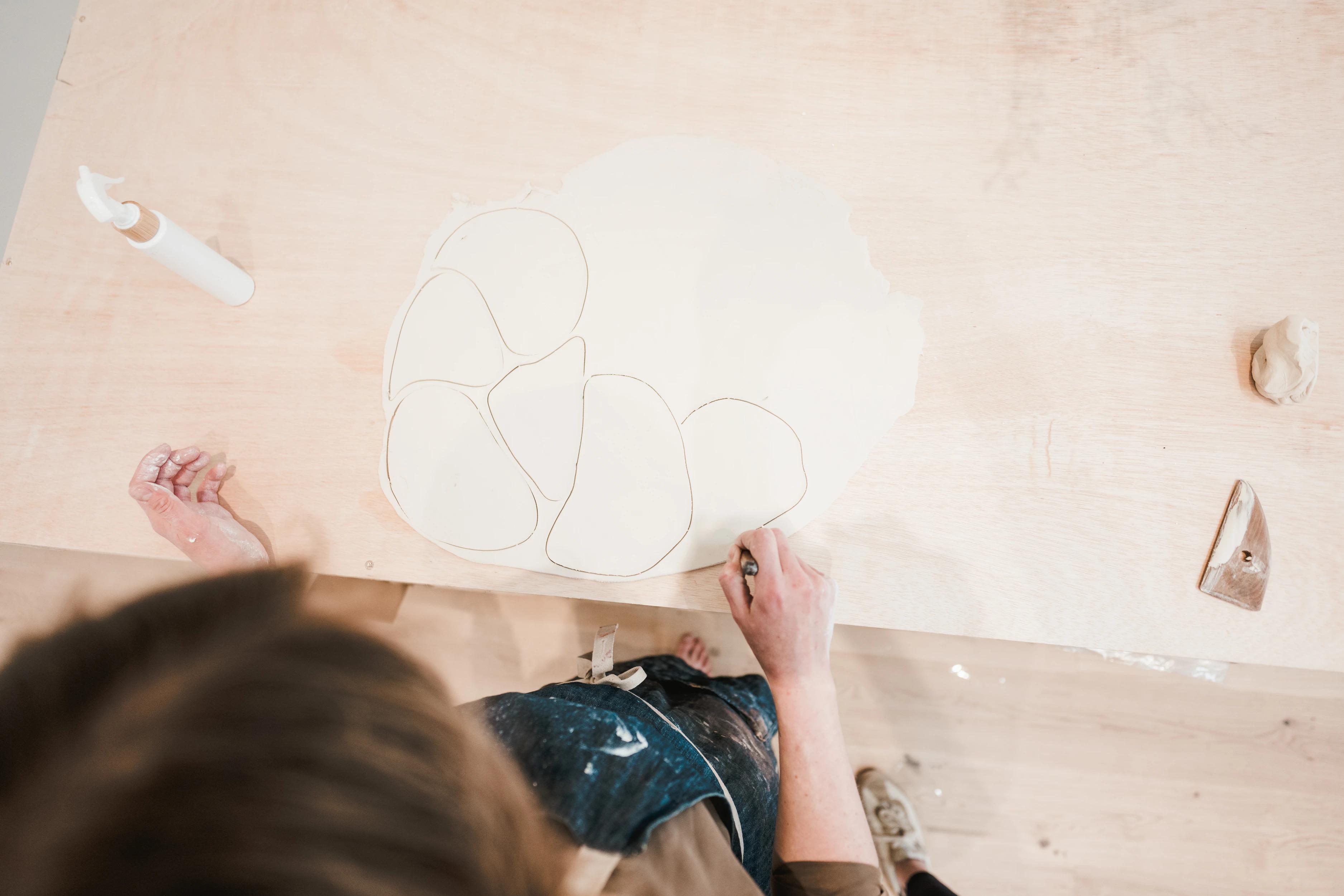 Artist Christina Watka cutting irregularly-shaped clay discs in her studio.