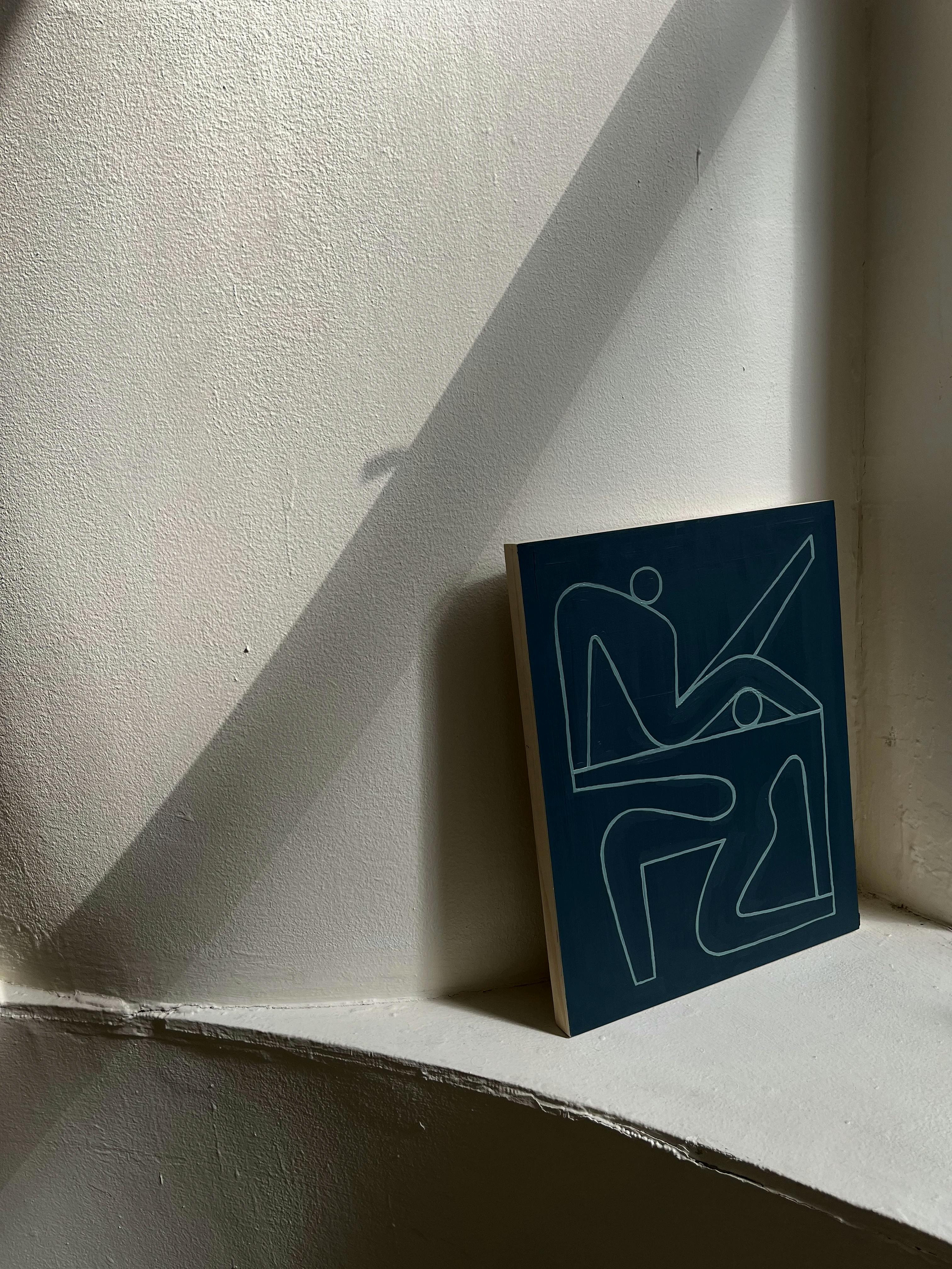 A blue painting of two abstract figures by artist Lourenço Providência positioned on a white ledge.