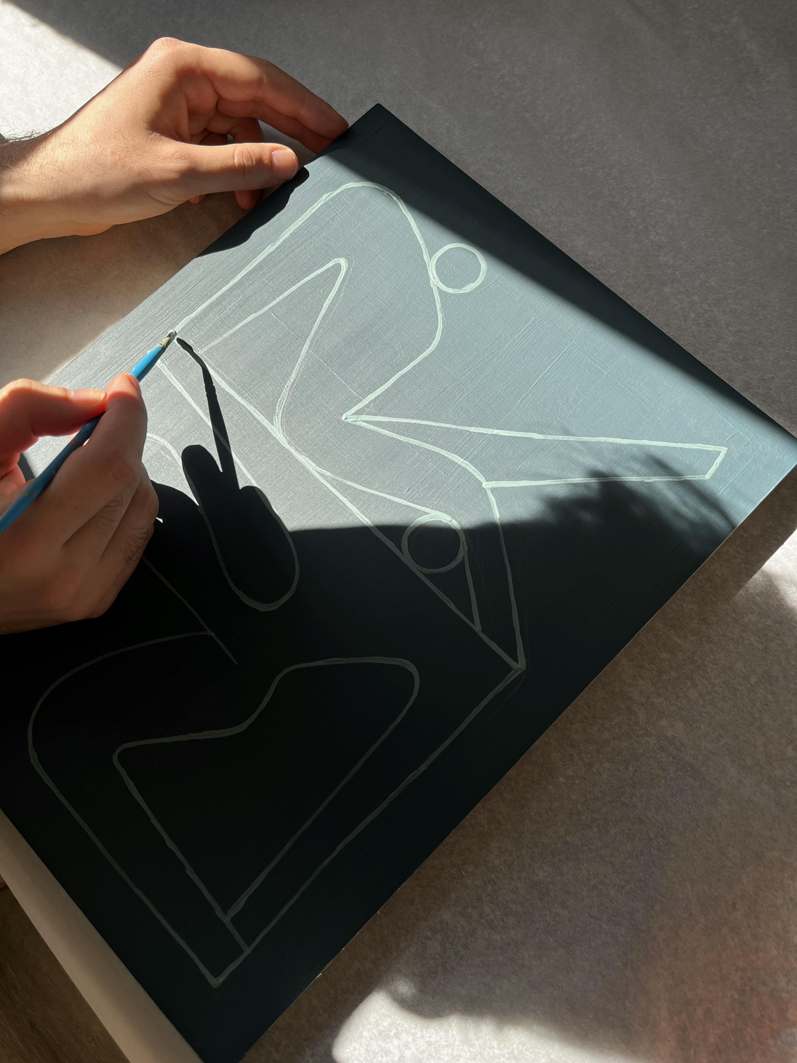 Artist Lourenço Providência working on a slate gray painting of abstract figures.