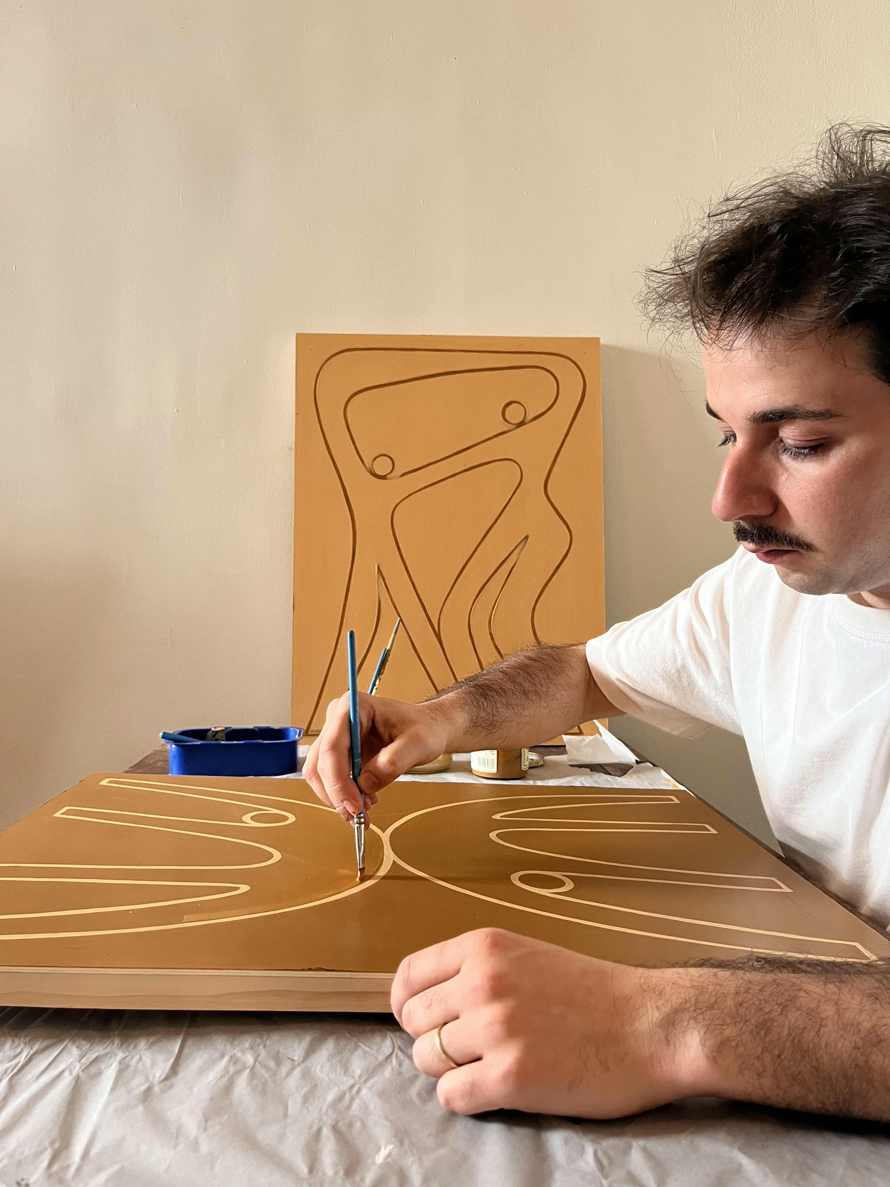 Artist Lourenço Providência working on an orange painting of entangled figures in his studio.