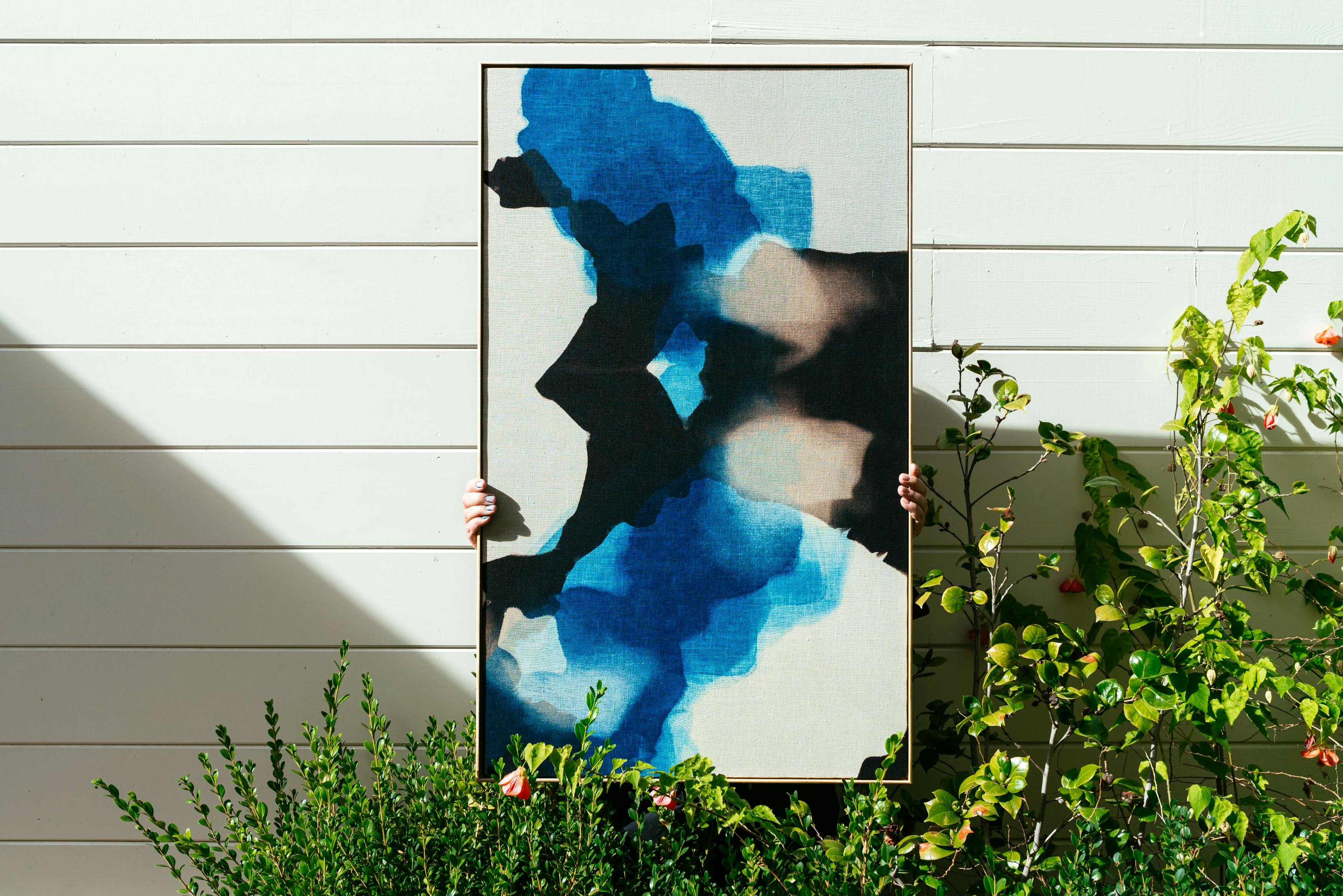 Artist Carrie Crawford holding up a naturally-dyed white and indigo artwork on the grounds of MacArthur Place.