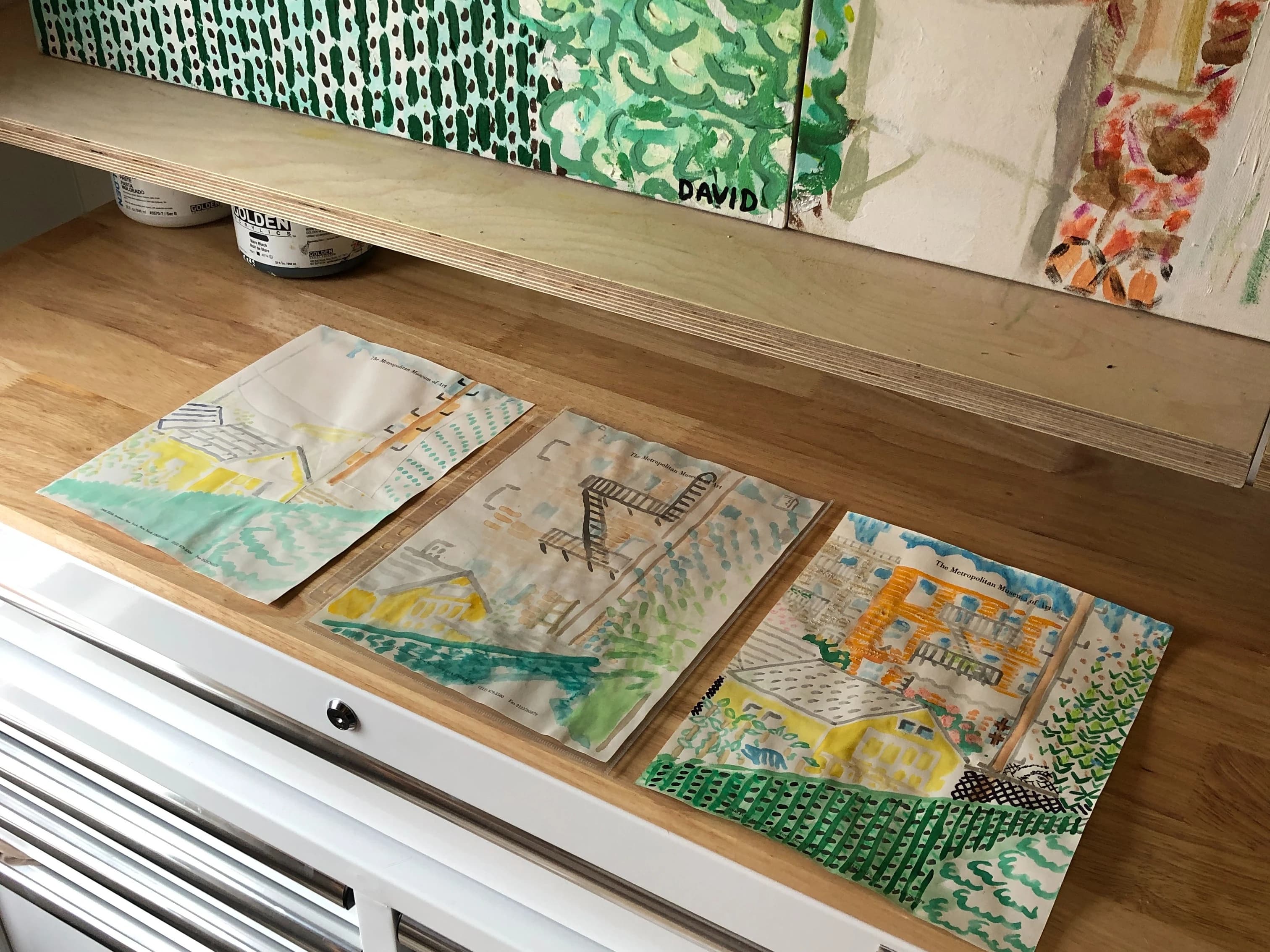 Landscape watercolor paintings by artist David Rhoads laid out on a wooden table in his studio.