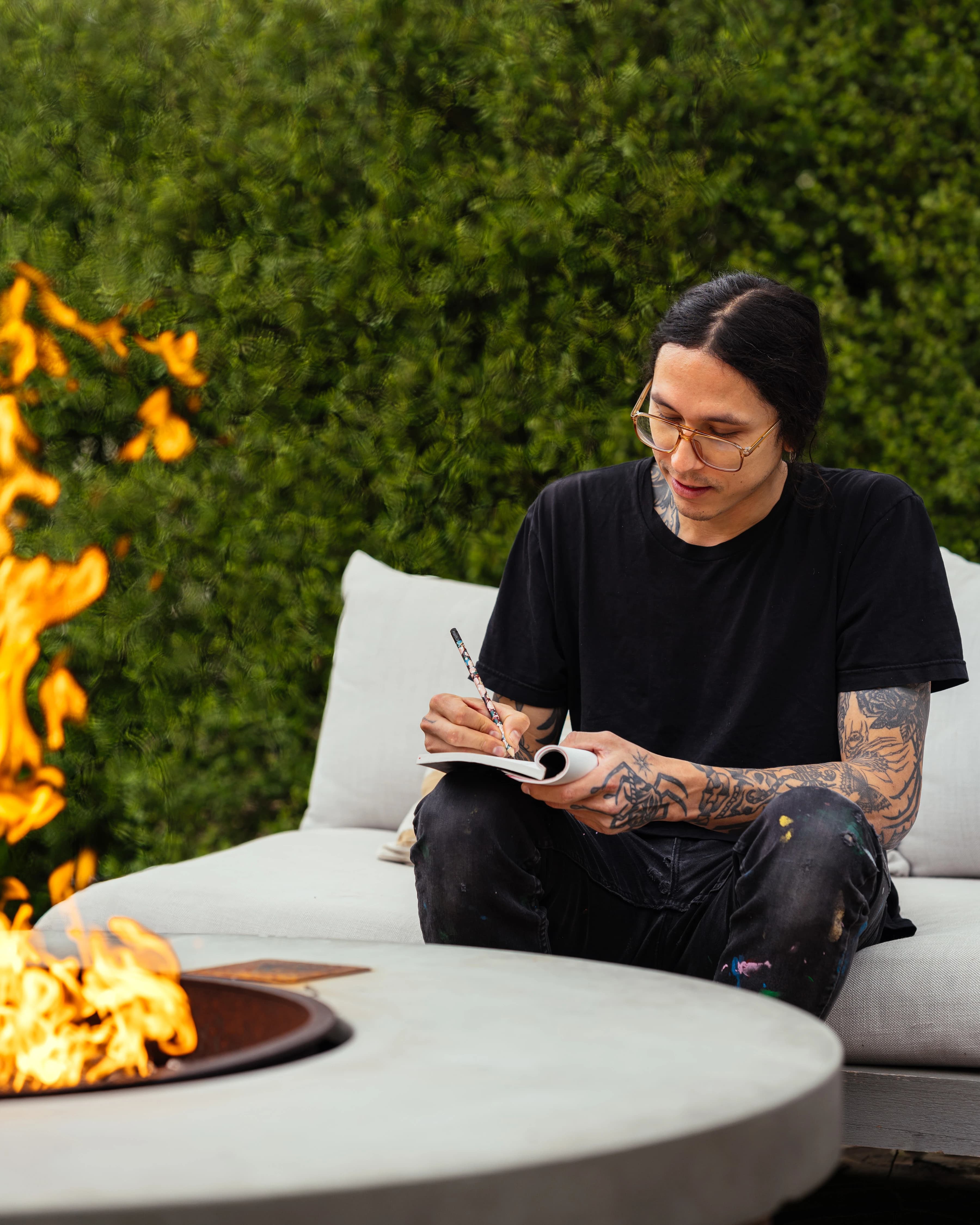 Artist Eddie Perrote sketching while sitting next to an outdoor fire pit on the Sonoma grounds during his Uprise Art x MacArthur Place Residency.