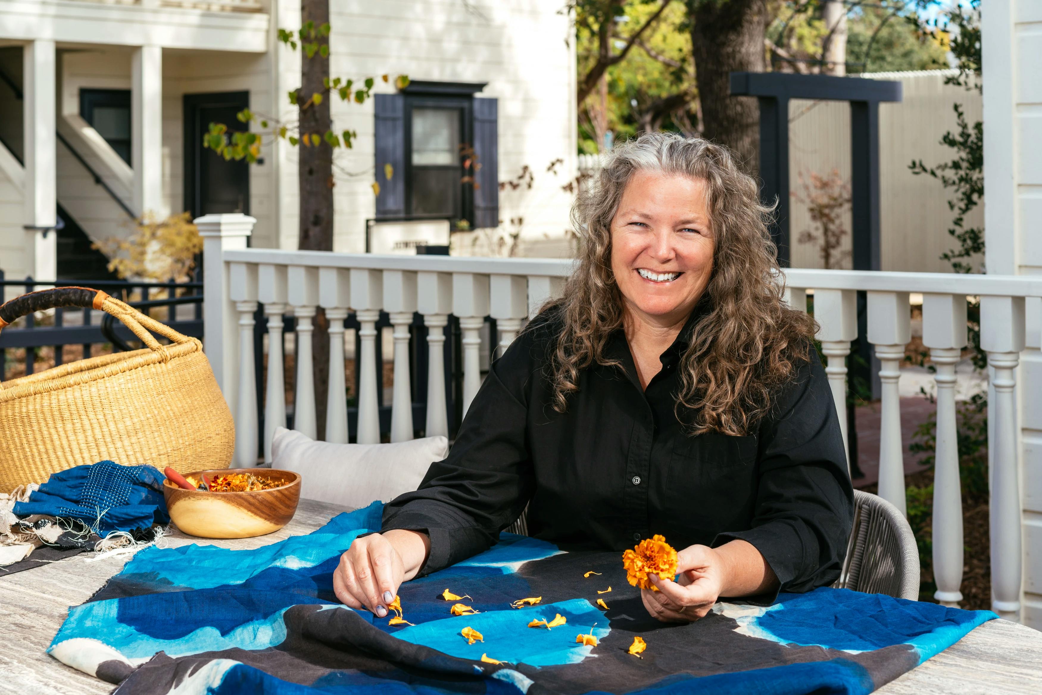 Artist Carrie Crawford sitting at a table on the Sonoma grounds, holding an orange flower. 