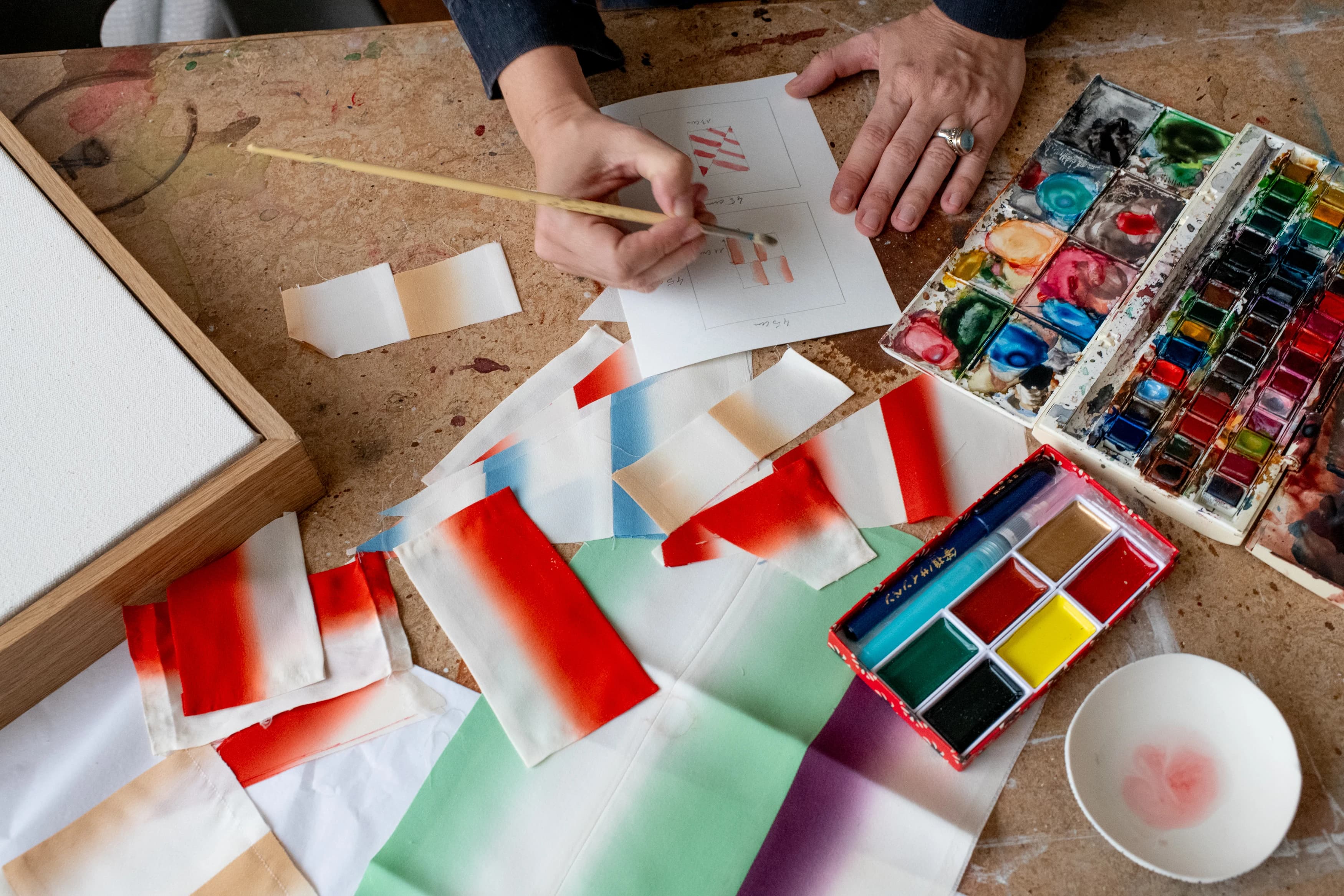 Artist Mada Vicassiau painting red and white patterns on paper in her studio.