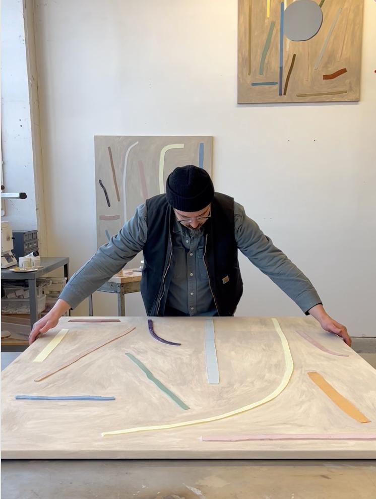 Artist J.C. Fontanive holding the edges of a large, abstract work on canvas in his studio.